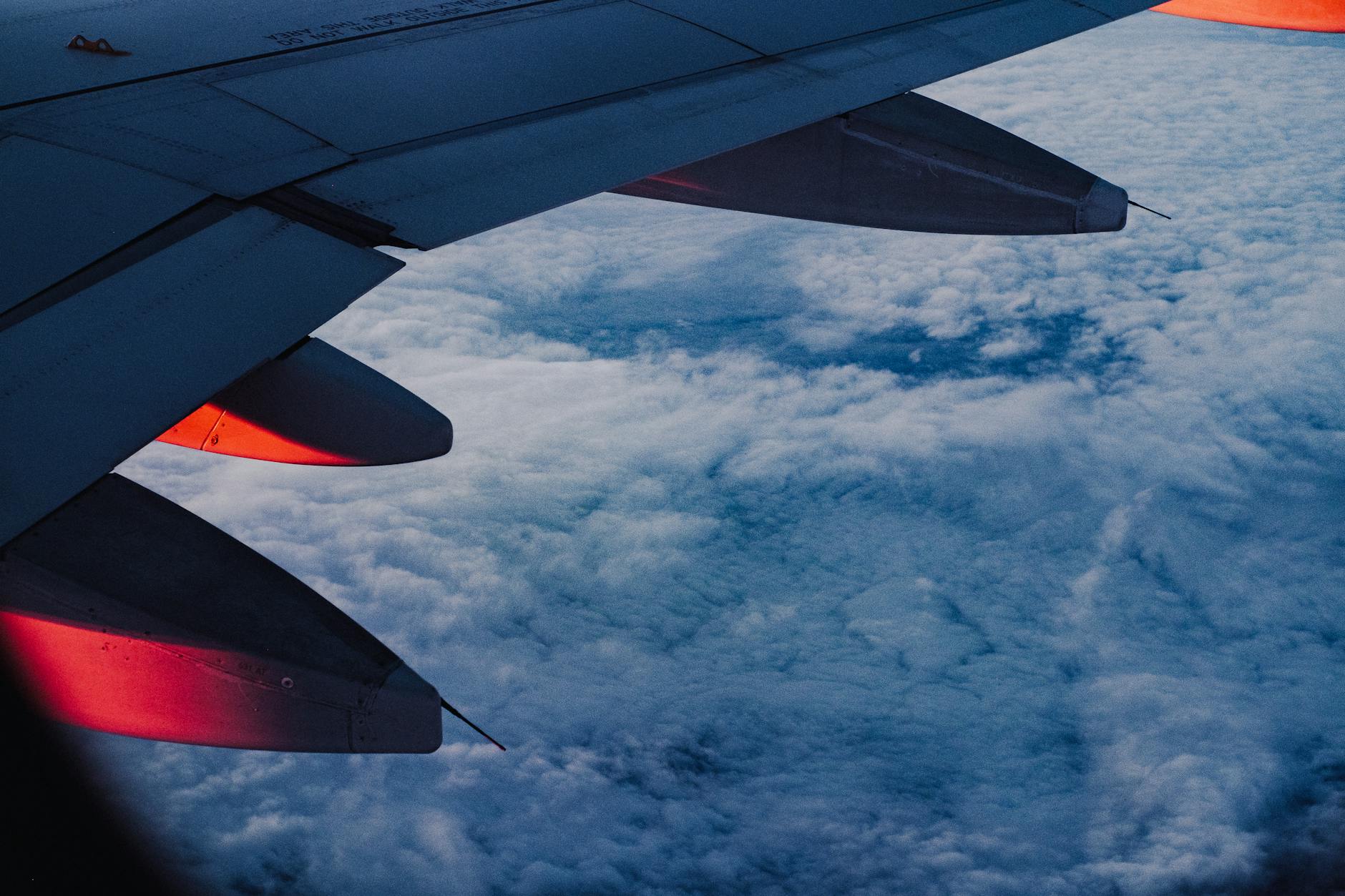 View from airplane window showing wing and clouds during flight over Europe