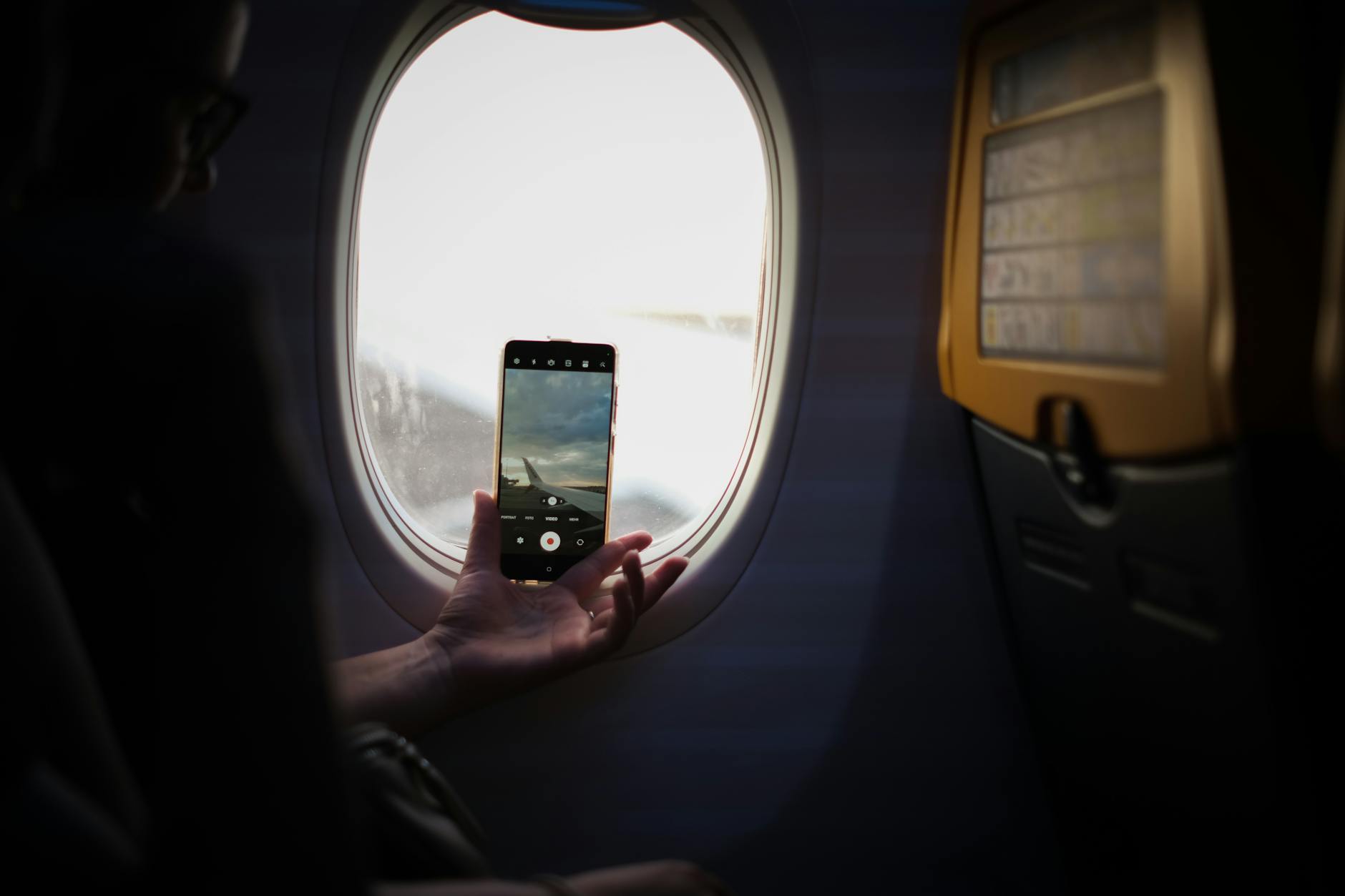 Hand holding smartphone with airline app open next to airplane window