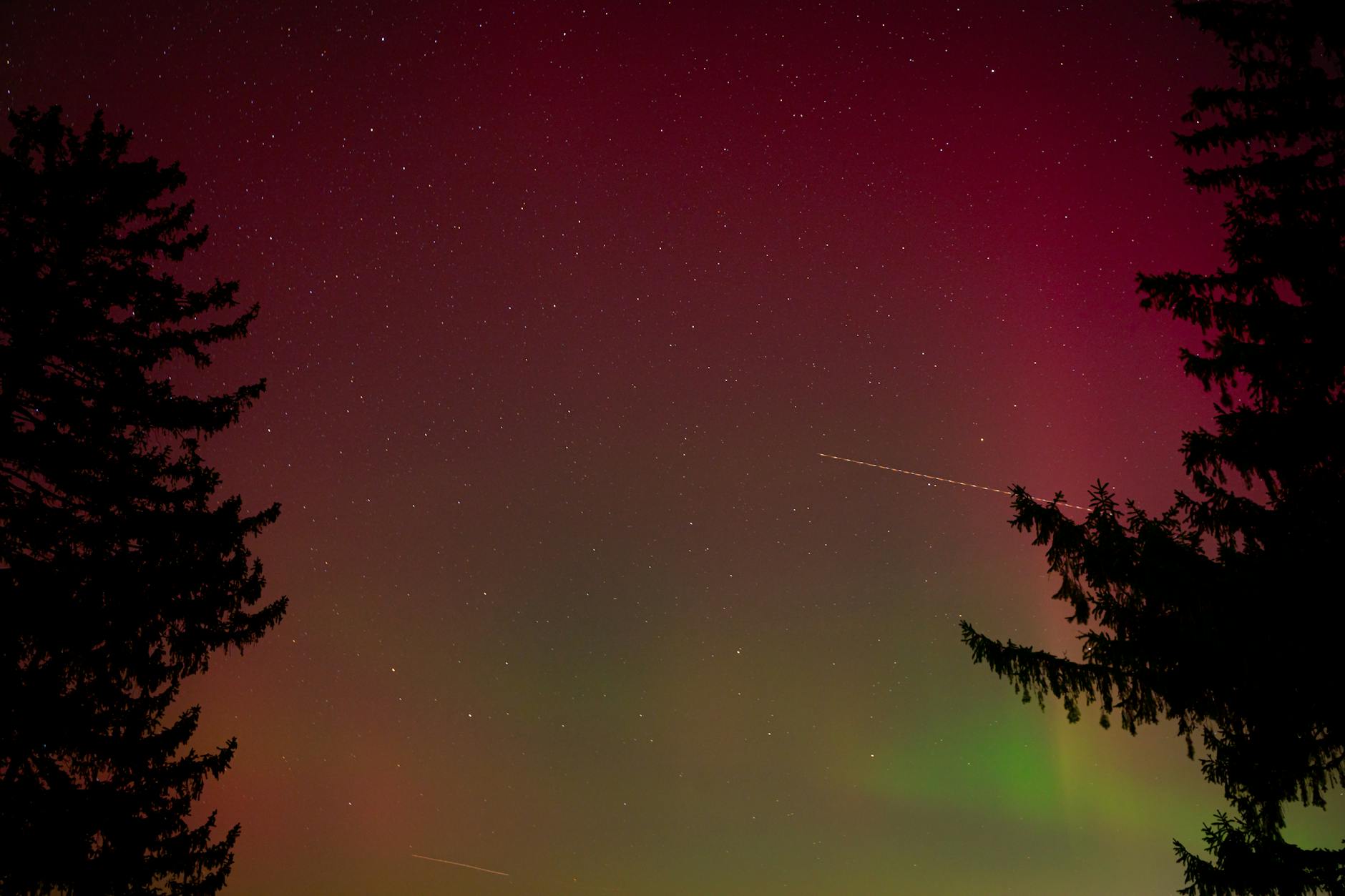 Green aurora borealis dancing across dark Arctic sky with silhouetted landscape