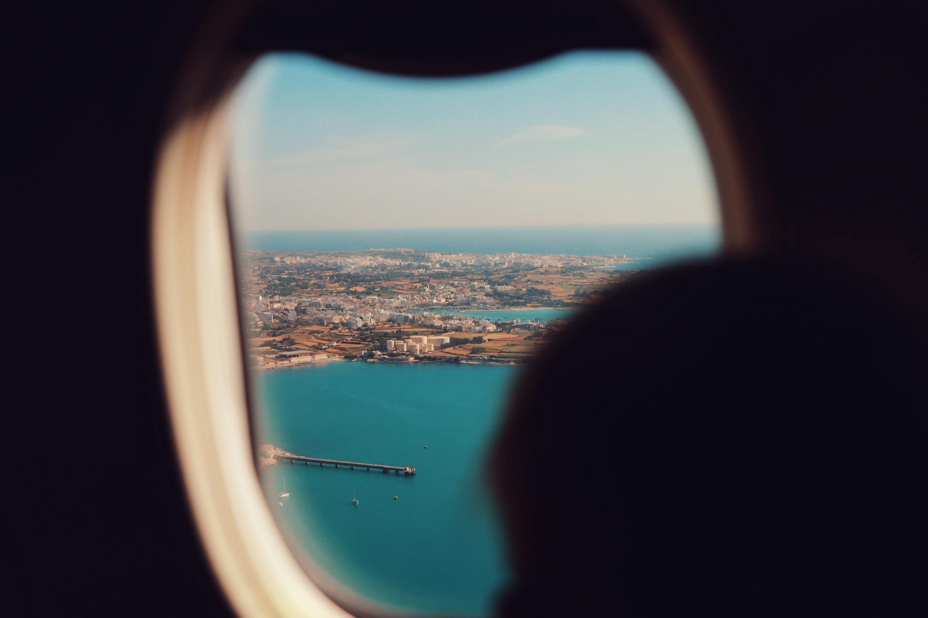 Passenger view through airplane window showing clouds and landscape below during flight