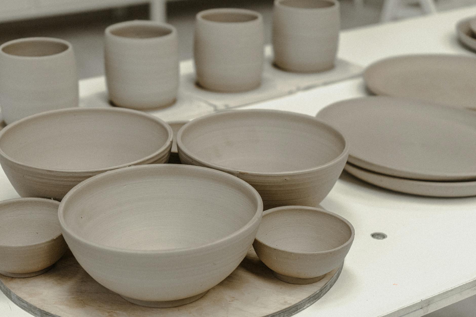 Hands working clay on pottery wheel in rustic workshop setting with art supplies