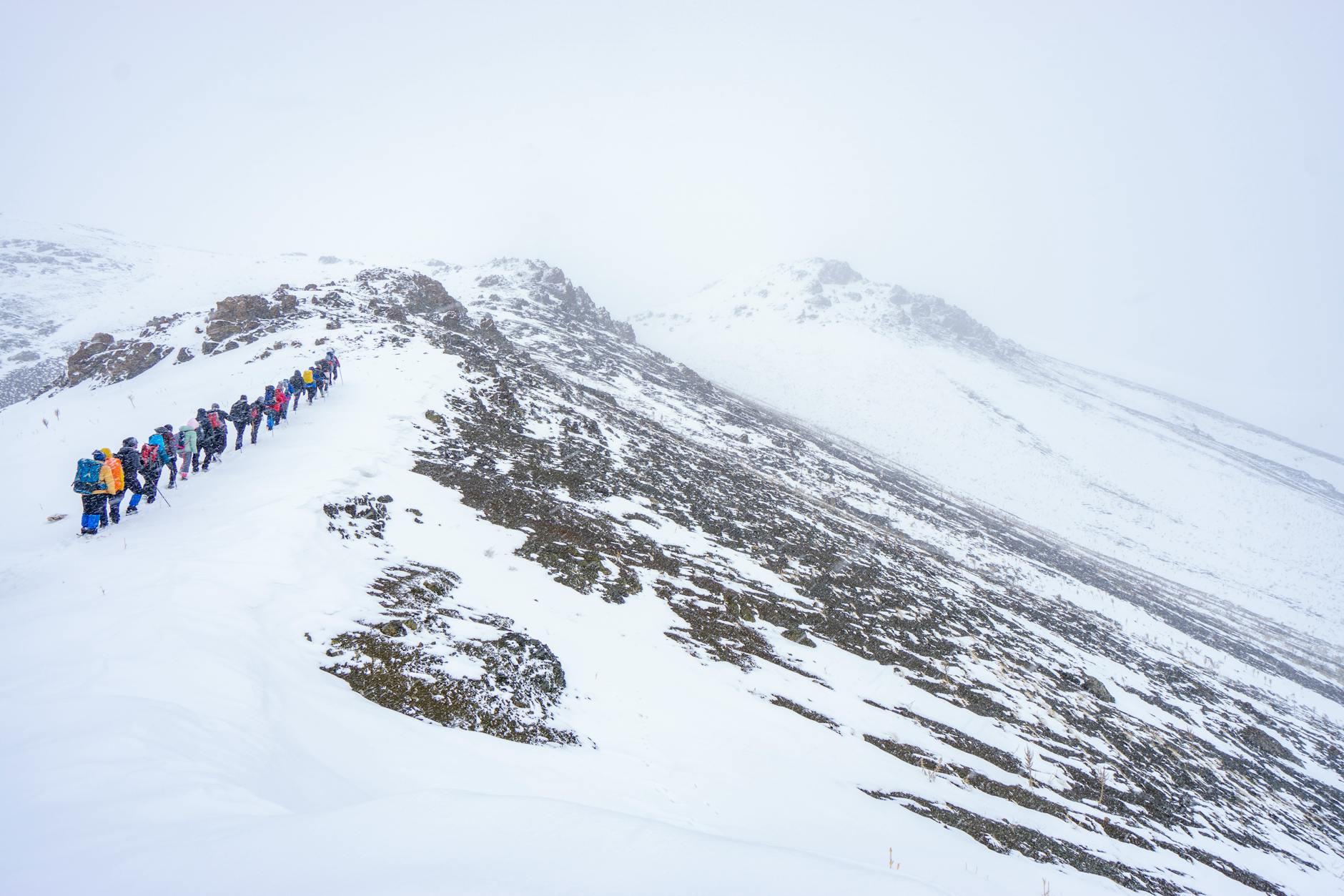 Winter hikers traversing snowy mountain trail with hiking poles and backpacks