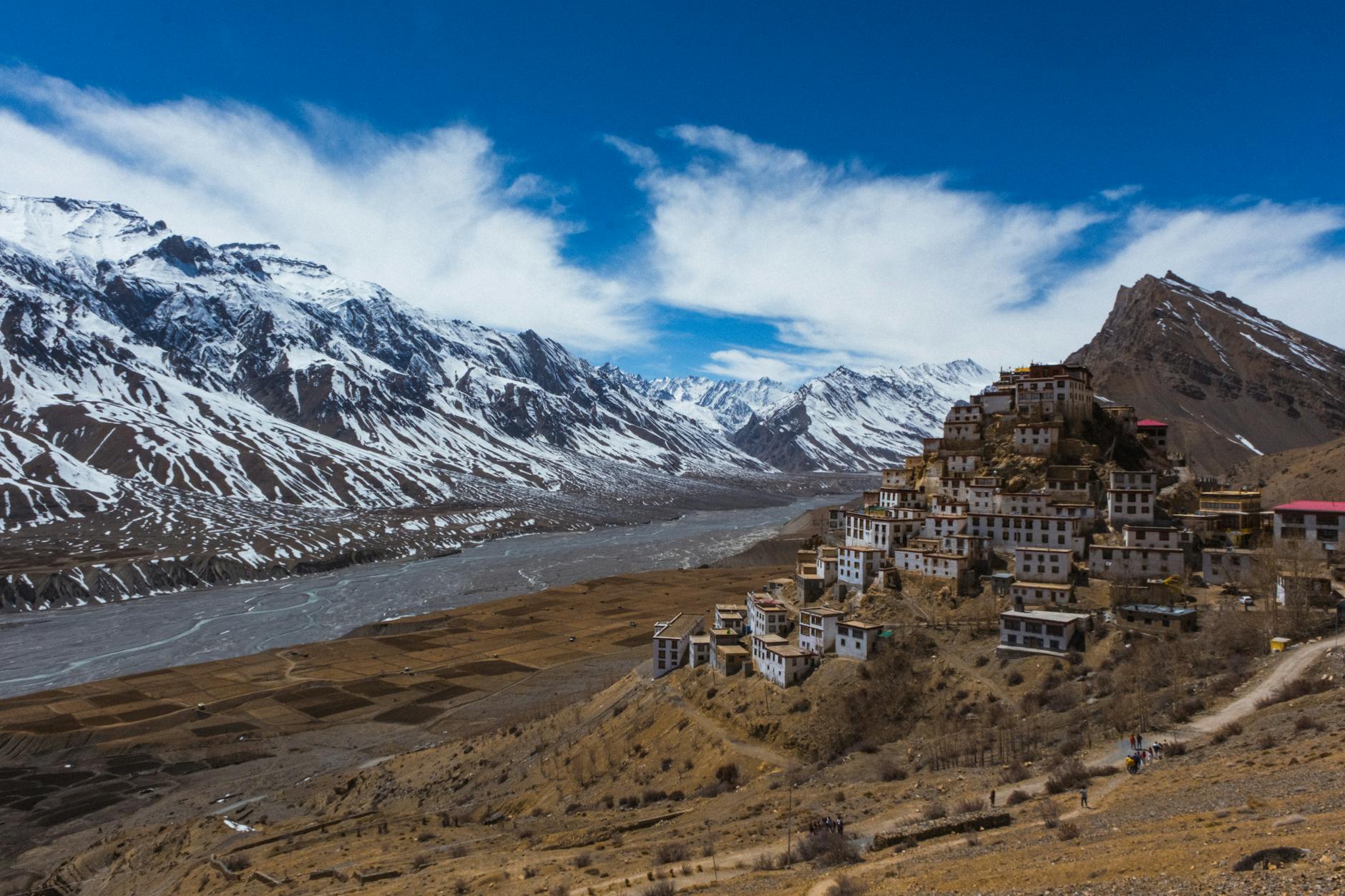 Buddhist monastery perched on cliff face overlooking mountain valley with prayer flags