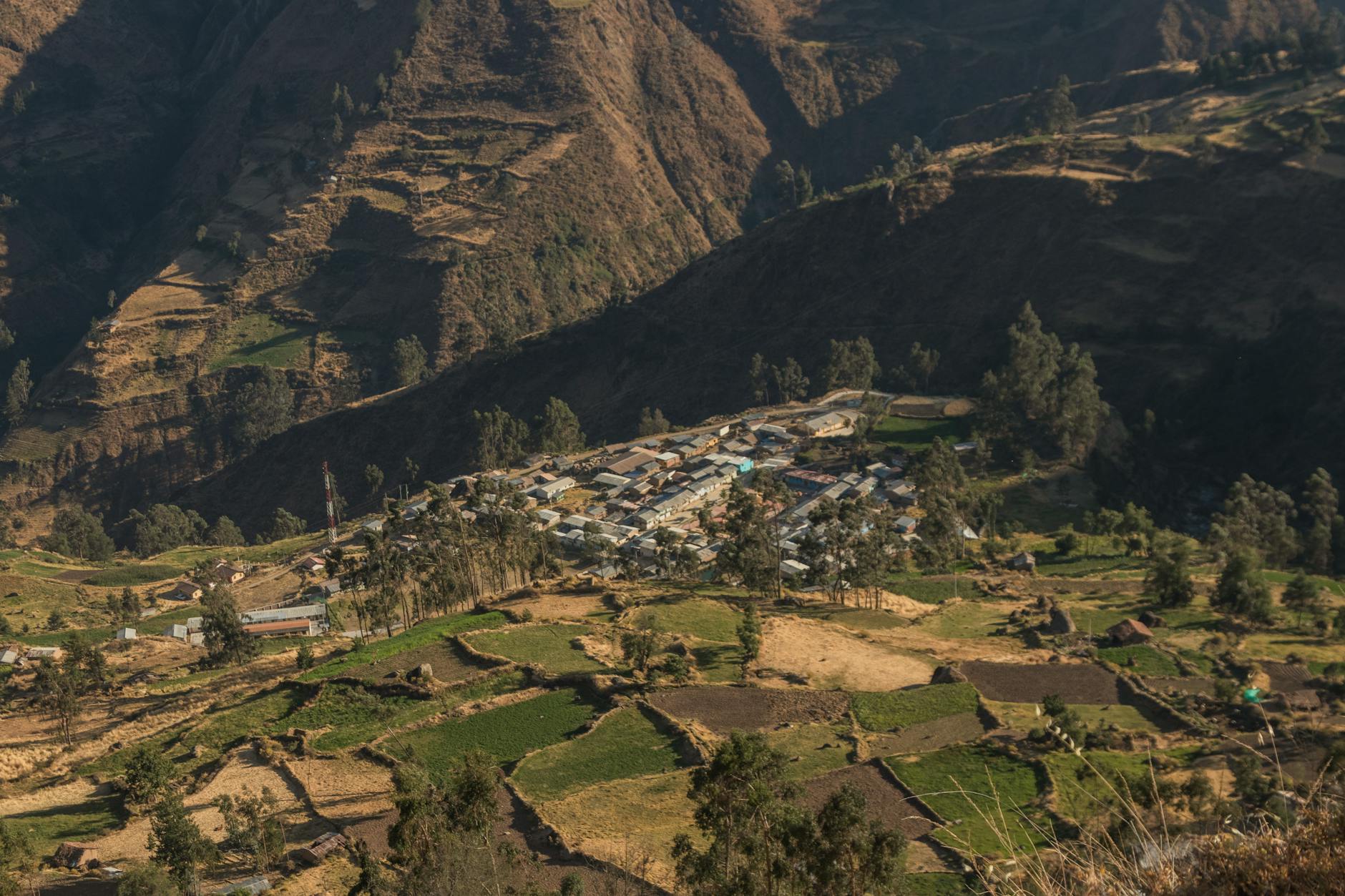 Traditional Andean village nestled in Sacred Valley mountains with adobe houses and terraced landscape