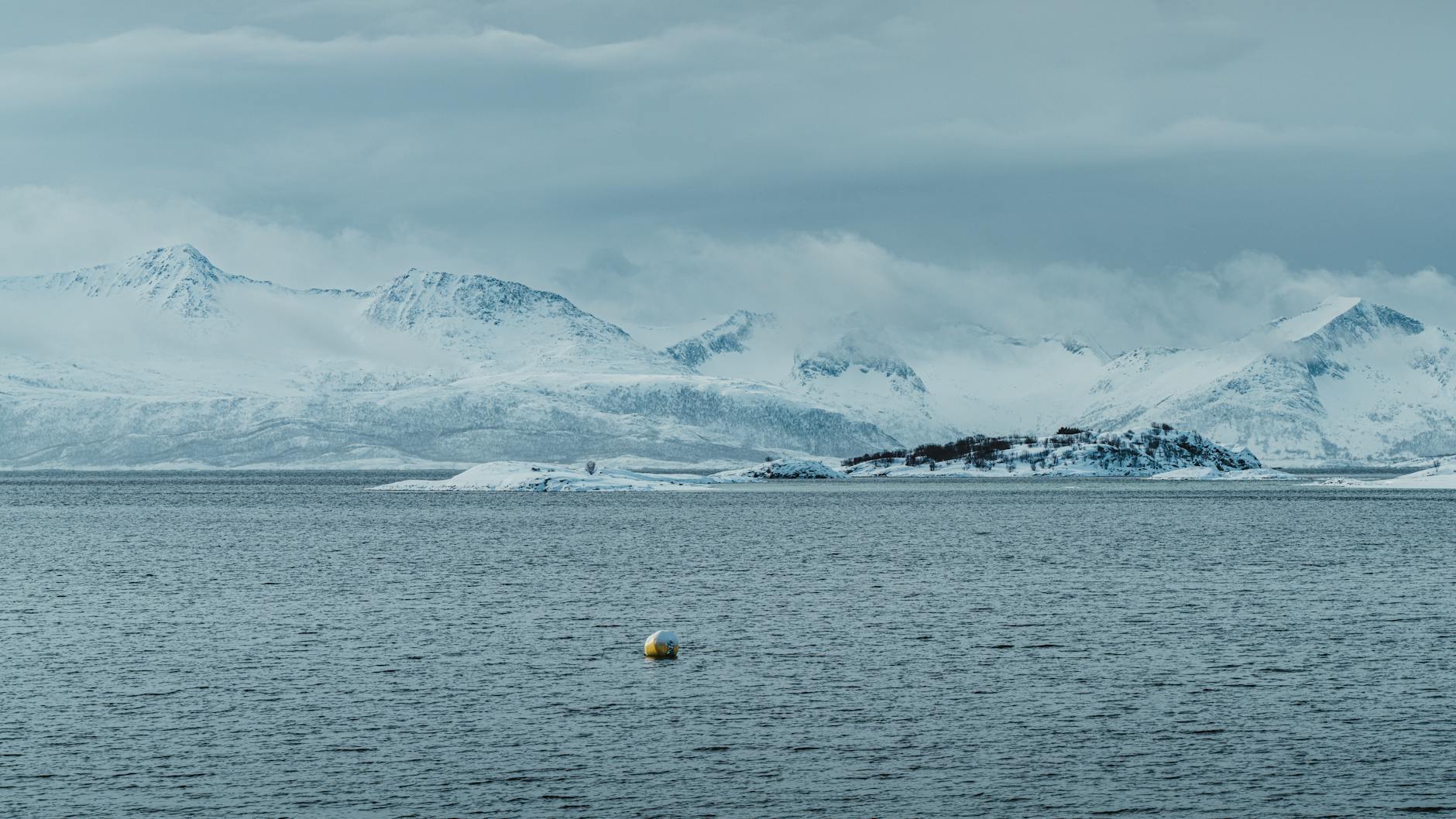 Snow-covered Arctic landscape with dramatic mountain peaks under winter sky