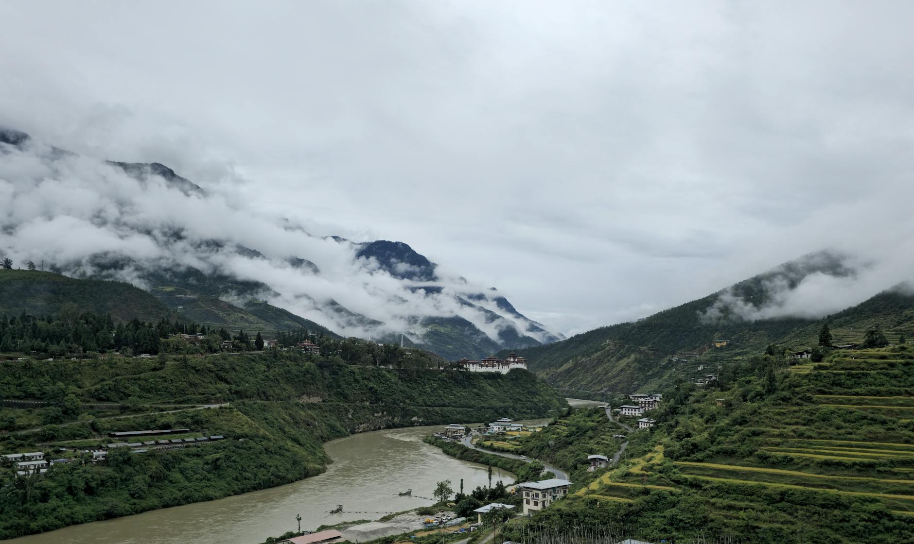 Scenic view of a lush Himalayan valley with traditional Bhutanese architecture surrounded by green hills