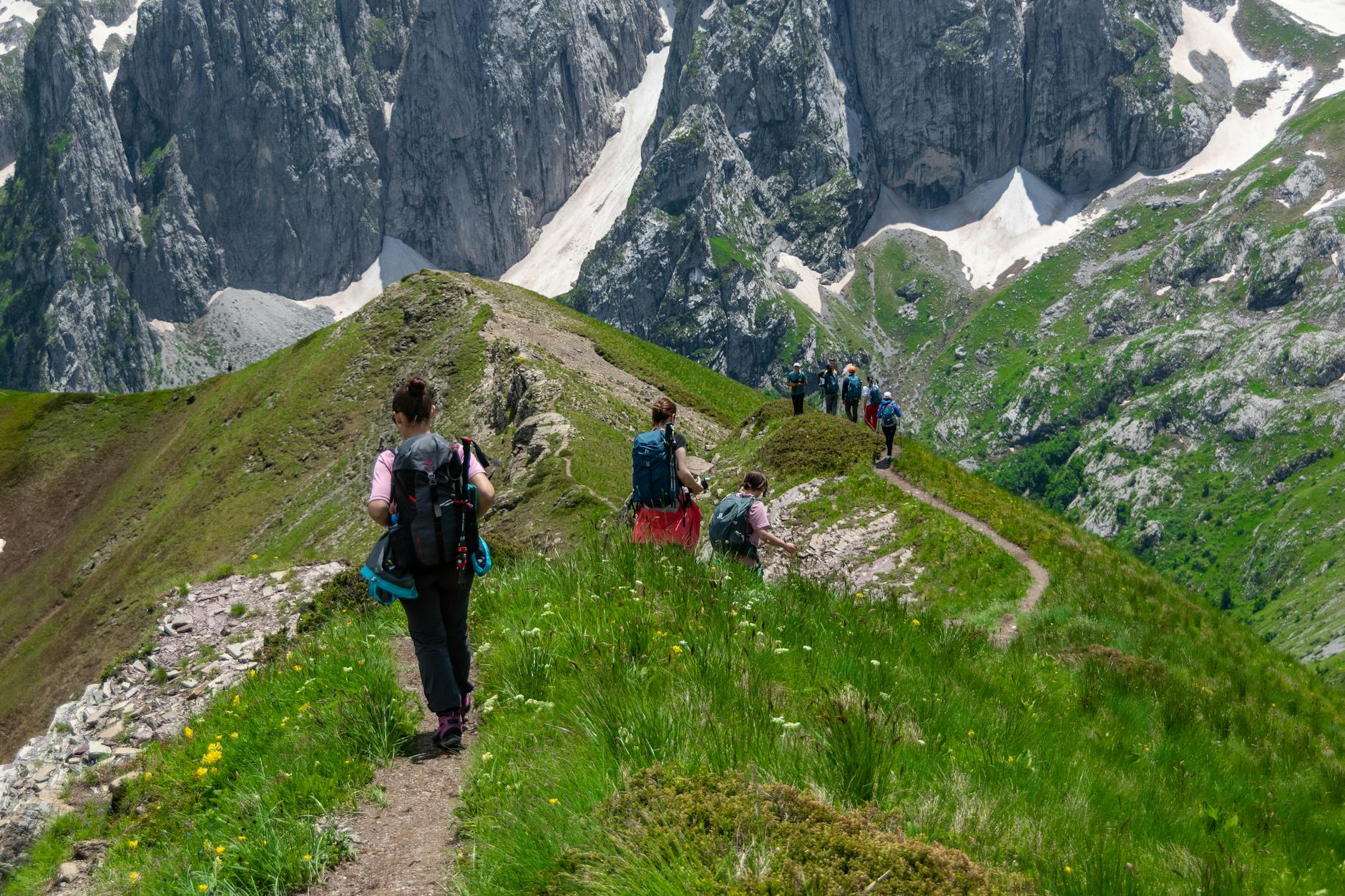 Hikers walking a narrow mountain trail with expansive landscape in the background