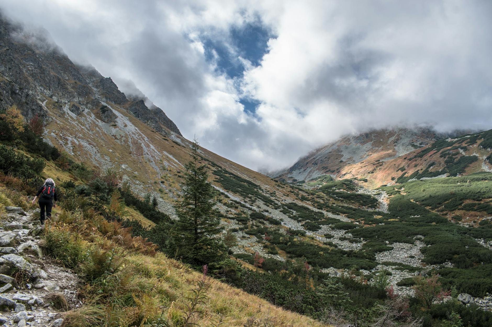 A hiker walking a narrow alpine trail with dramatic mountain scenery in the background