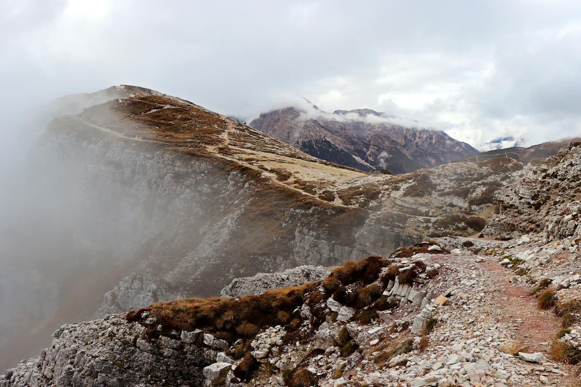 A hiker on a remote mountain trail partially obscured by low fog
