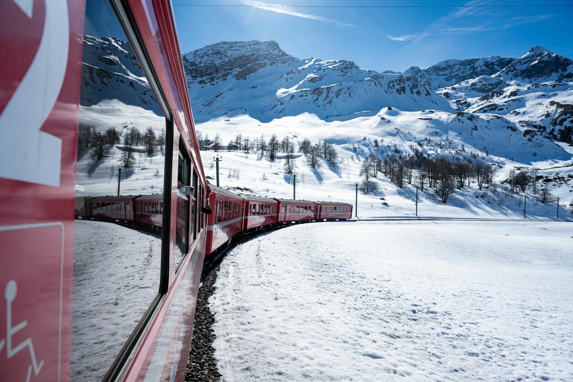 Passenger train traveling through mountainous terrain with snow-capped peaks in the background