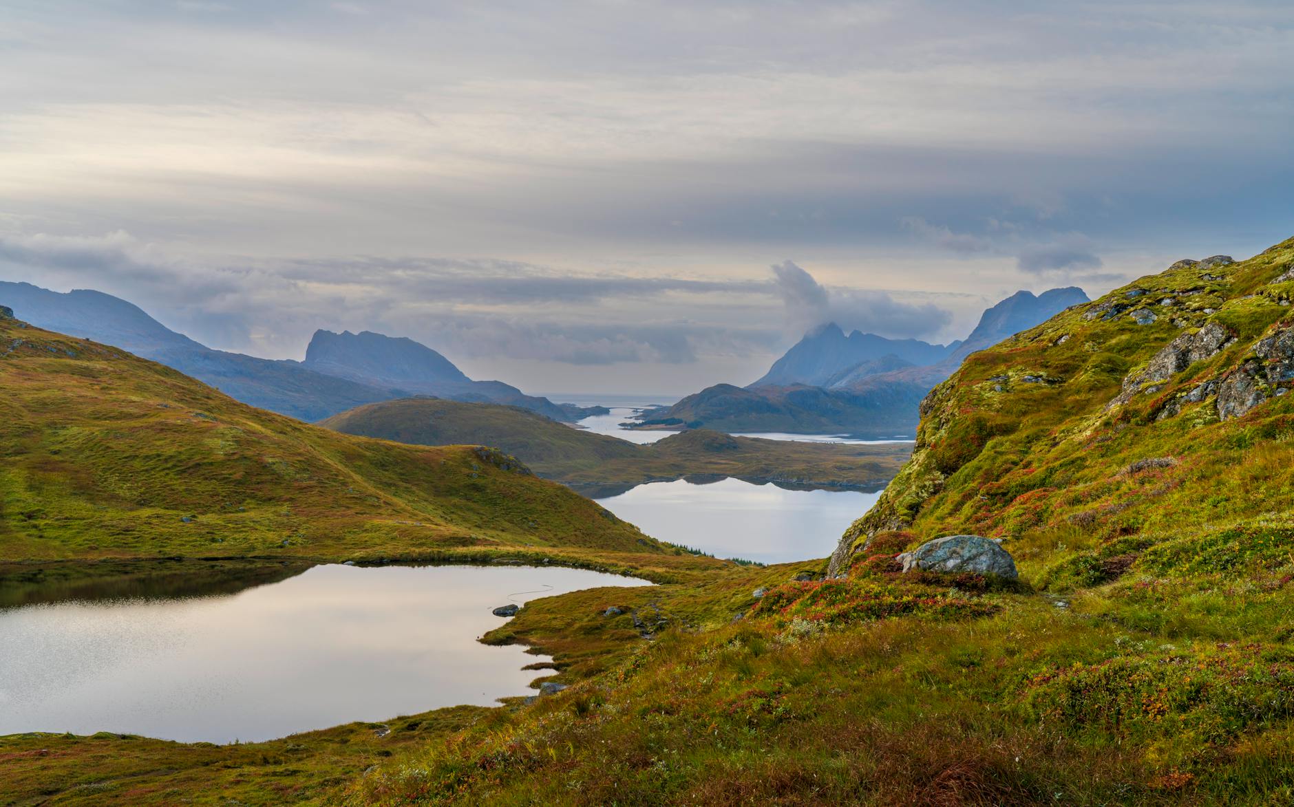 Still lake surrounded by rugged Nordic terrain under overcast skies