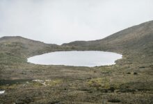 Green volcanic crater lake surrounded by Andean highlands under cloudy sky