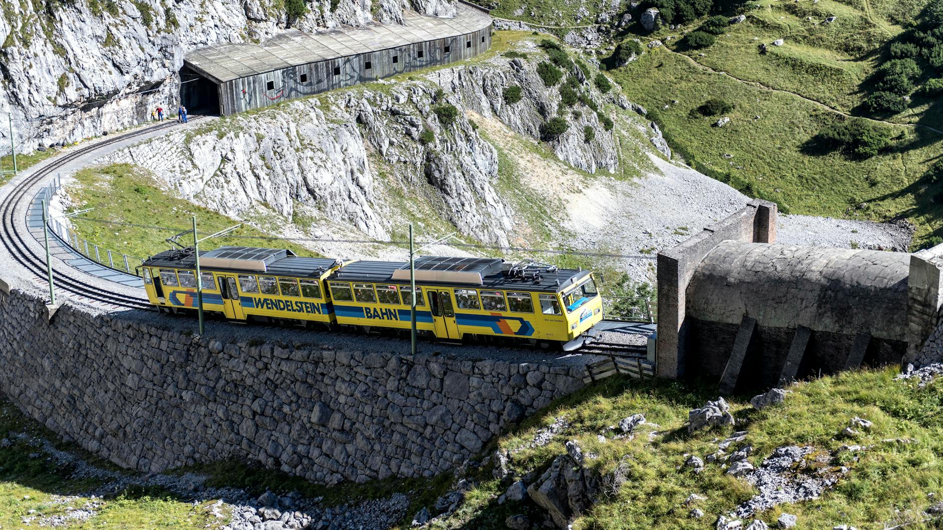 A passenger train moving through a misty mountain valley surrounded by green hillsides
