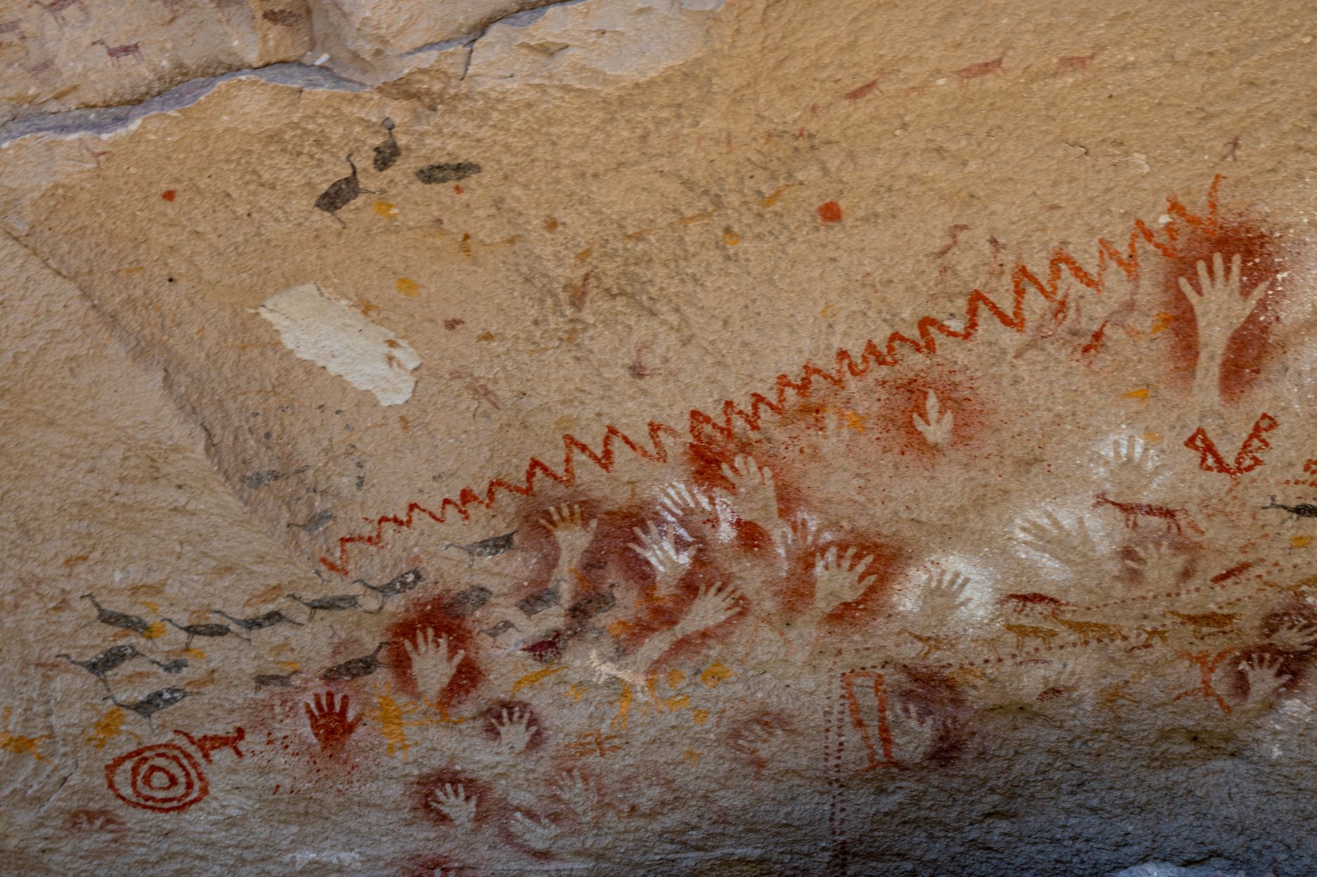 San rock art painted in ochre and white on a cave wall showing human and animal figures
