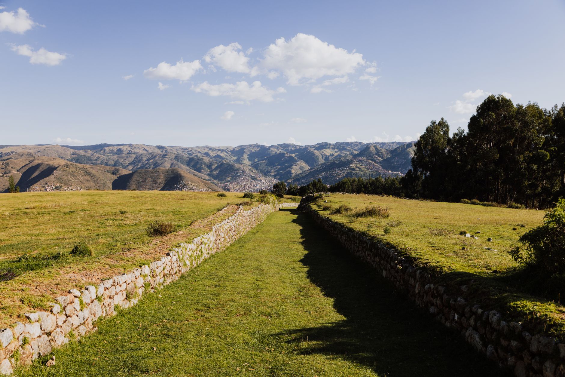 Narrow hiking trail through highland Andean farmland with mountain ridges in the background