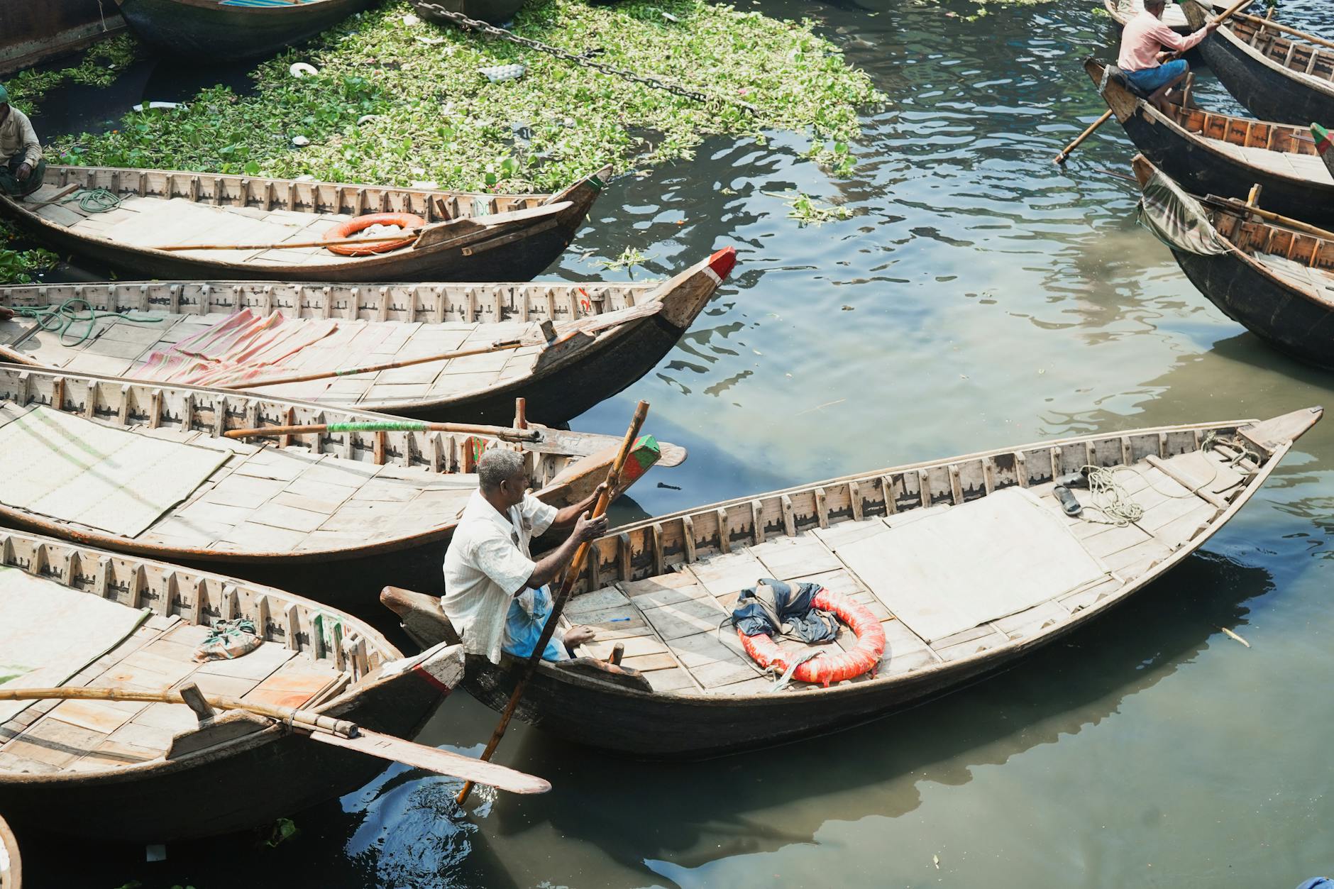Traditional wooden longboat gliding through narrow waterway surrounded by green vegetation