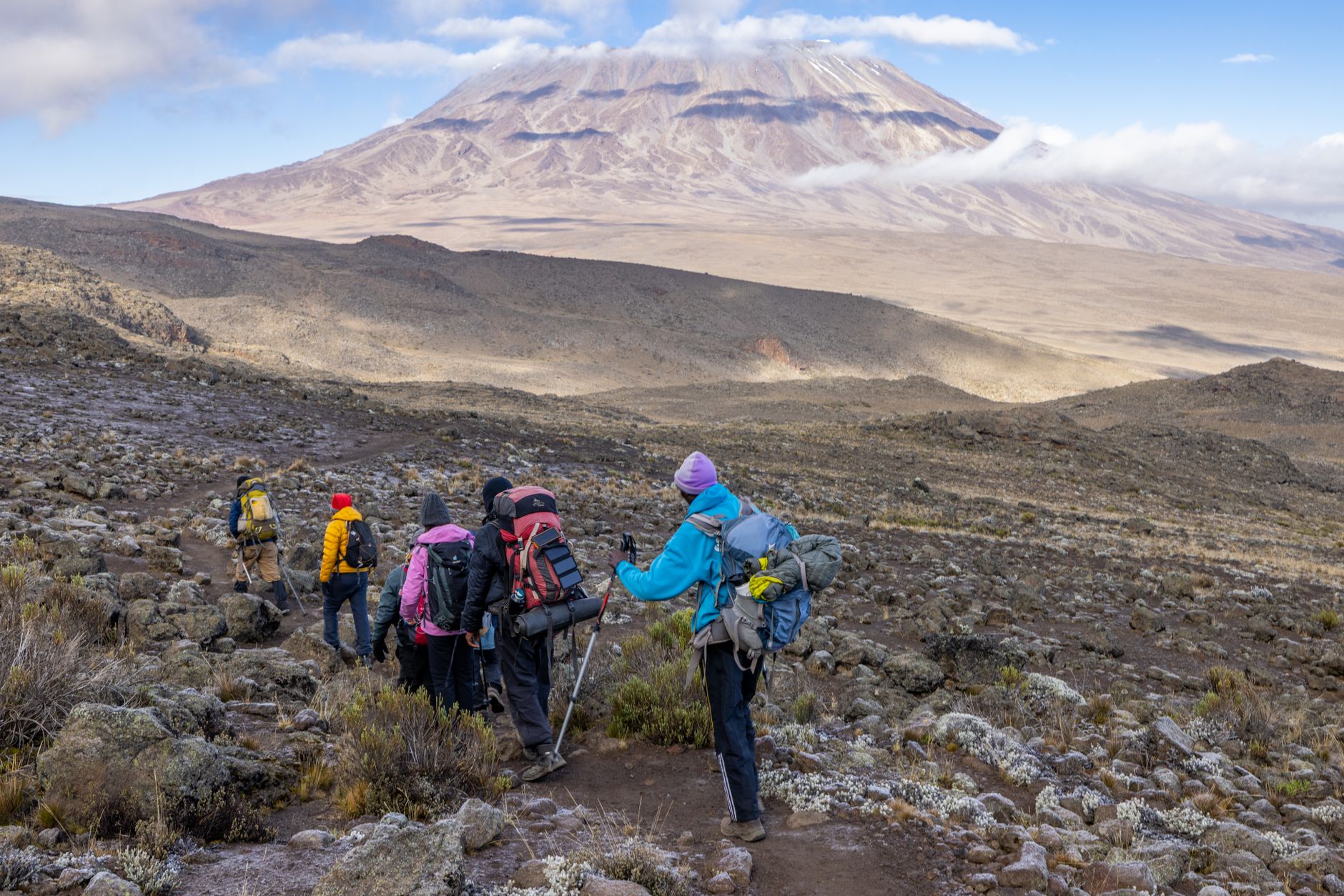 Solo trekker hiking through arid high-altitude desert terrain with volcanic mountains in the background
