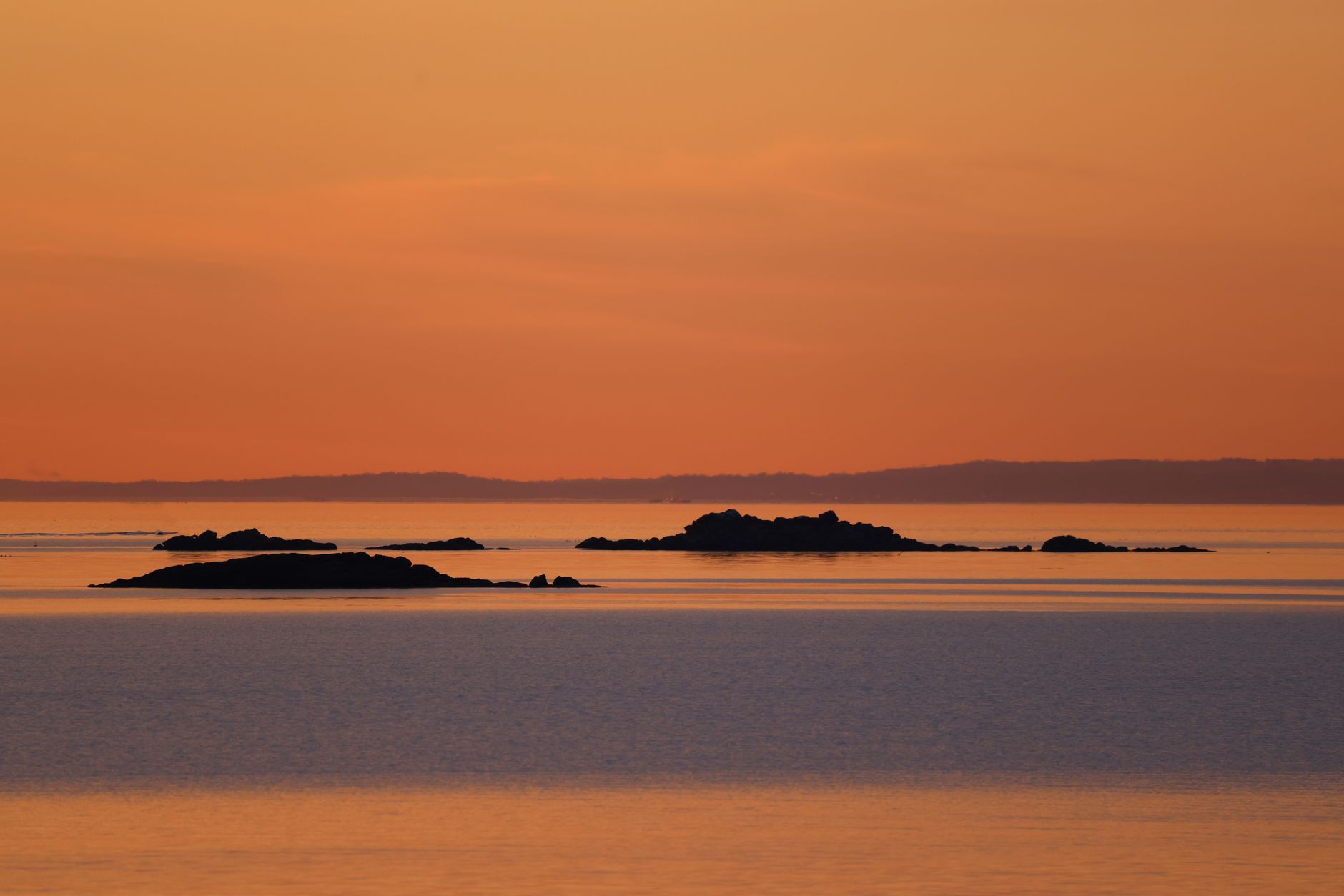 Sailboat anchored in a sheltered bay at sunset with rocky cliffs reflected in still water