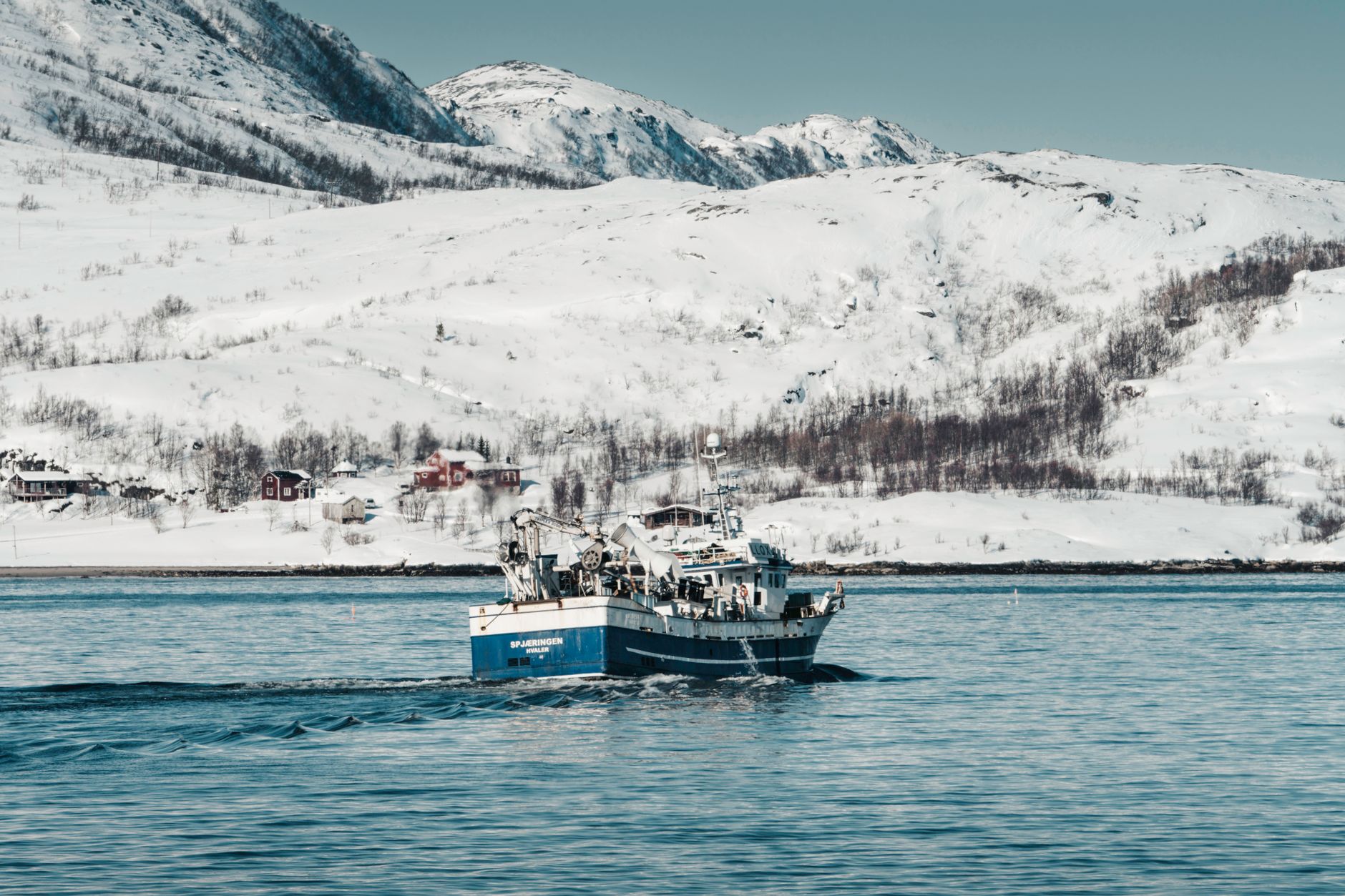 Small expedition boat navigating calm Arctic fjord waters surrounded by mountainous terrain