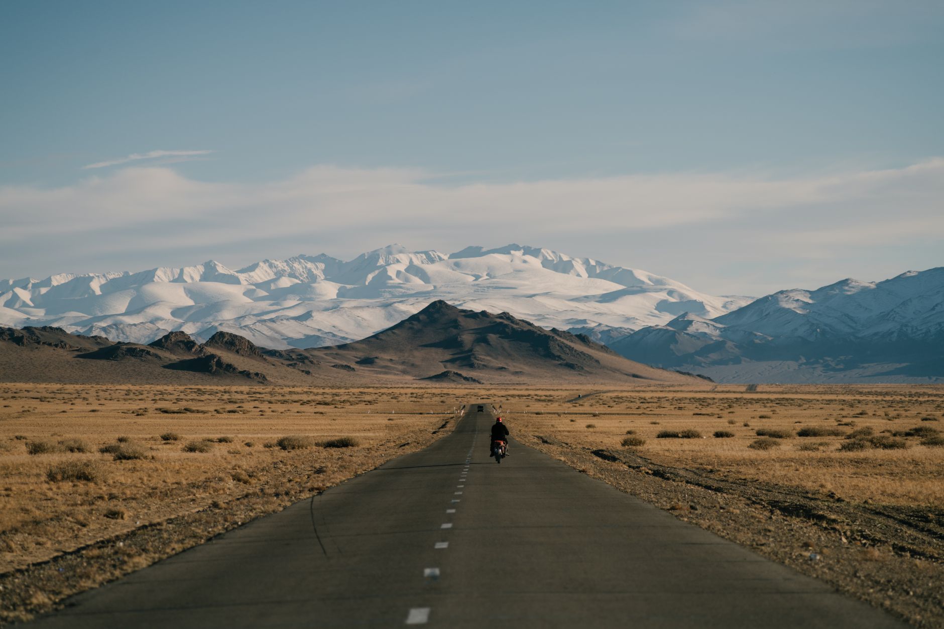 Empty desert road cutting through a dry valley landscape with mountains in the distance