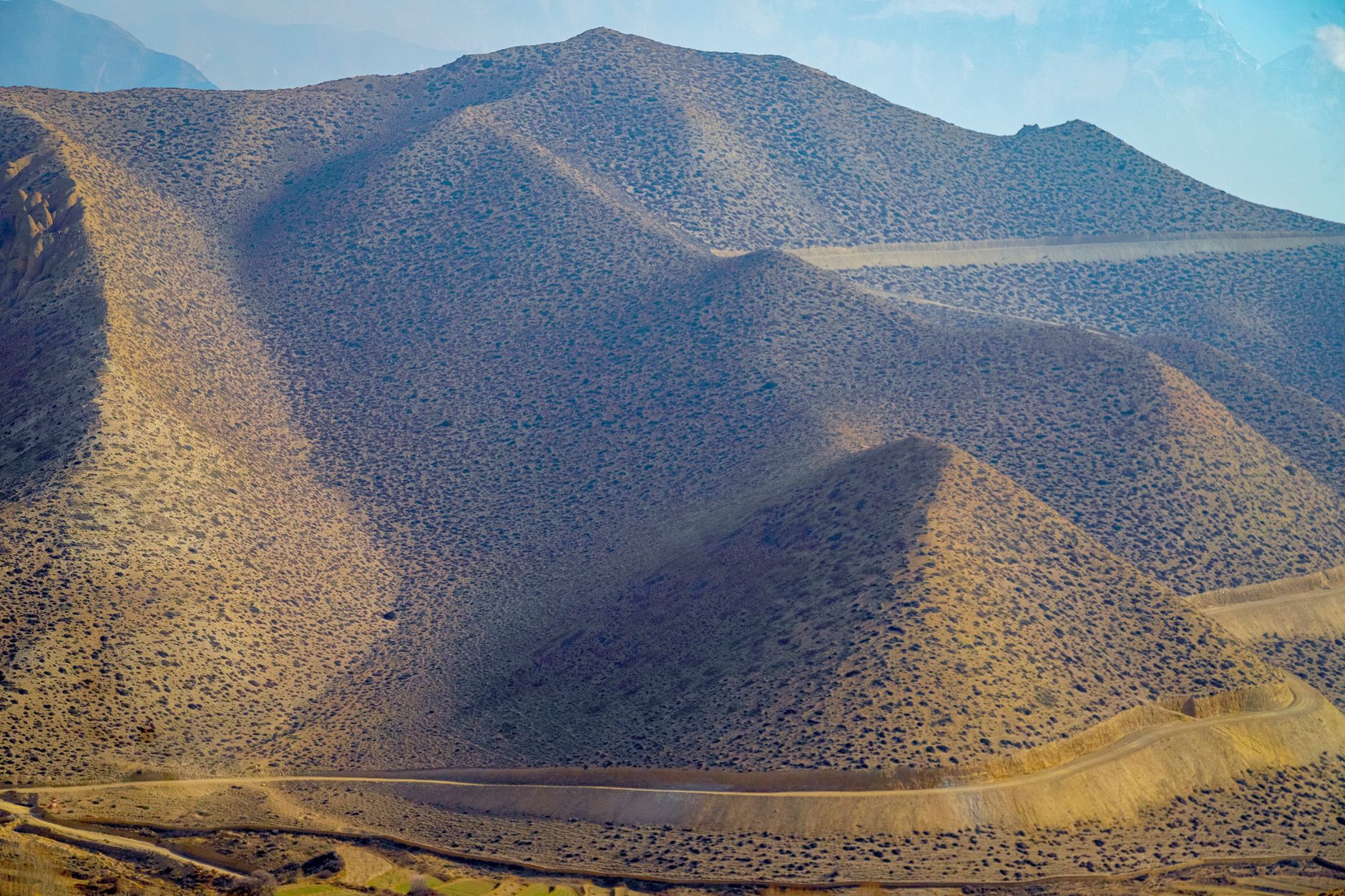 Trekker walking across a high-altitude arid plateau with eroded red and orange rock formations