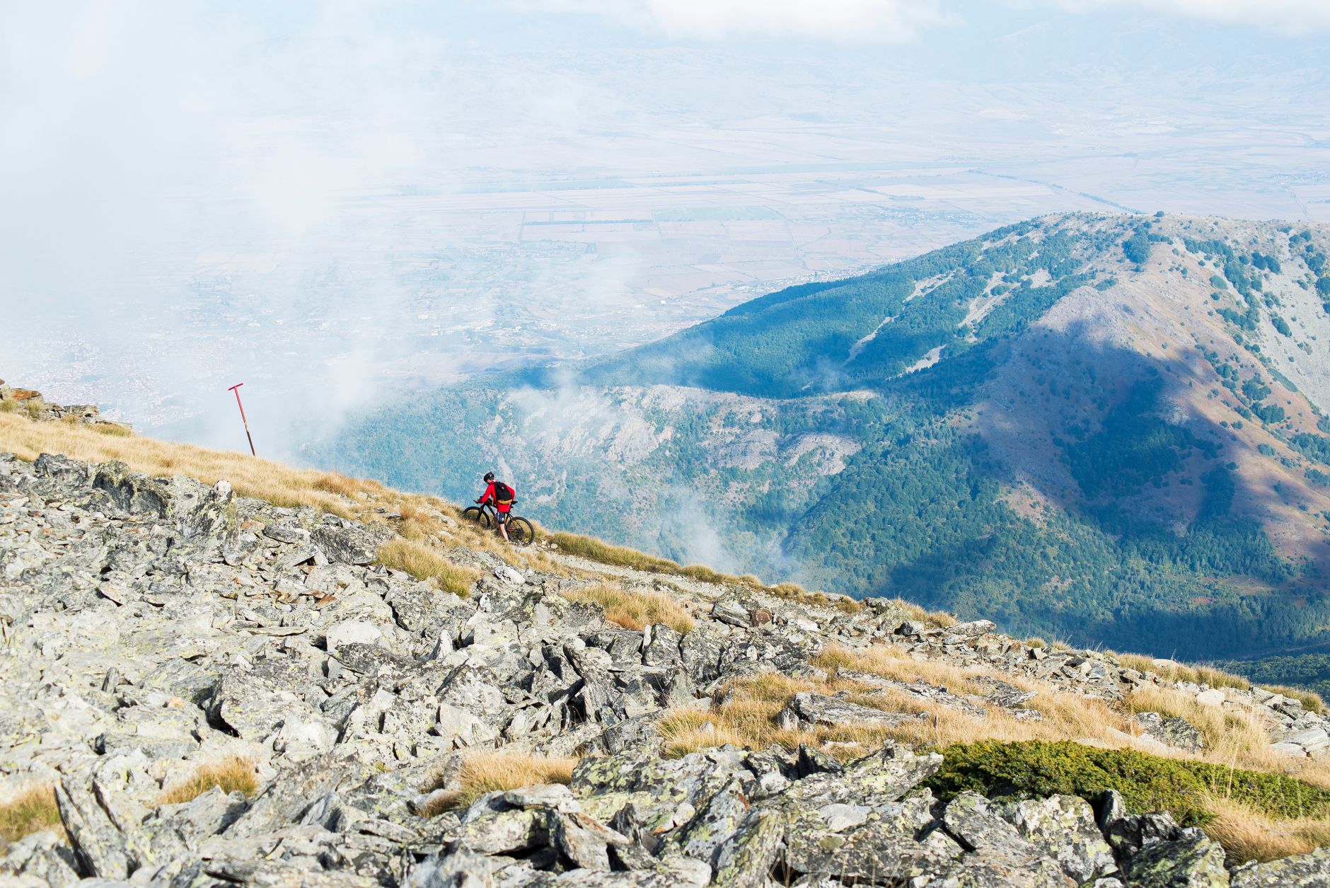 Cyclist riding along a narrow mountain trail with steep peaks in the background