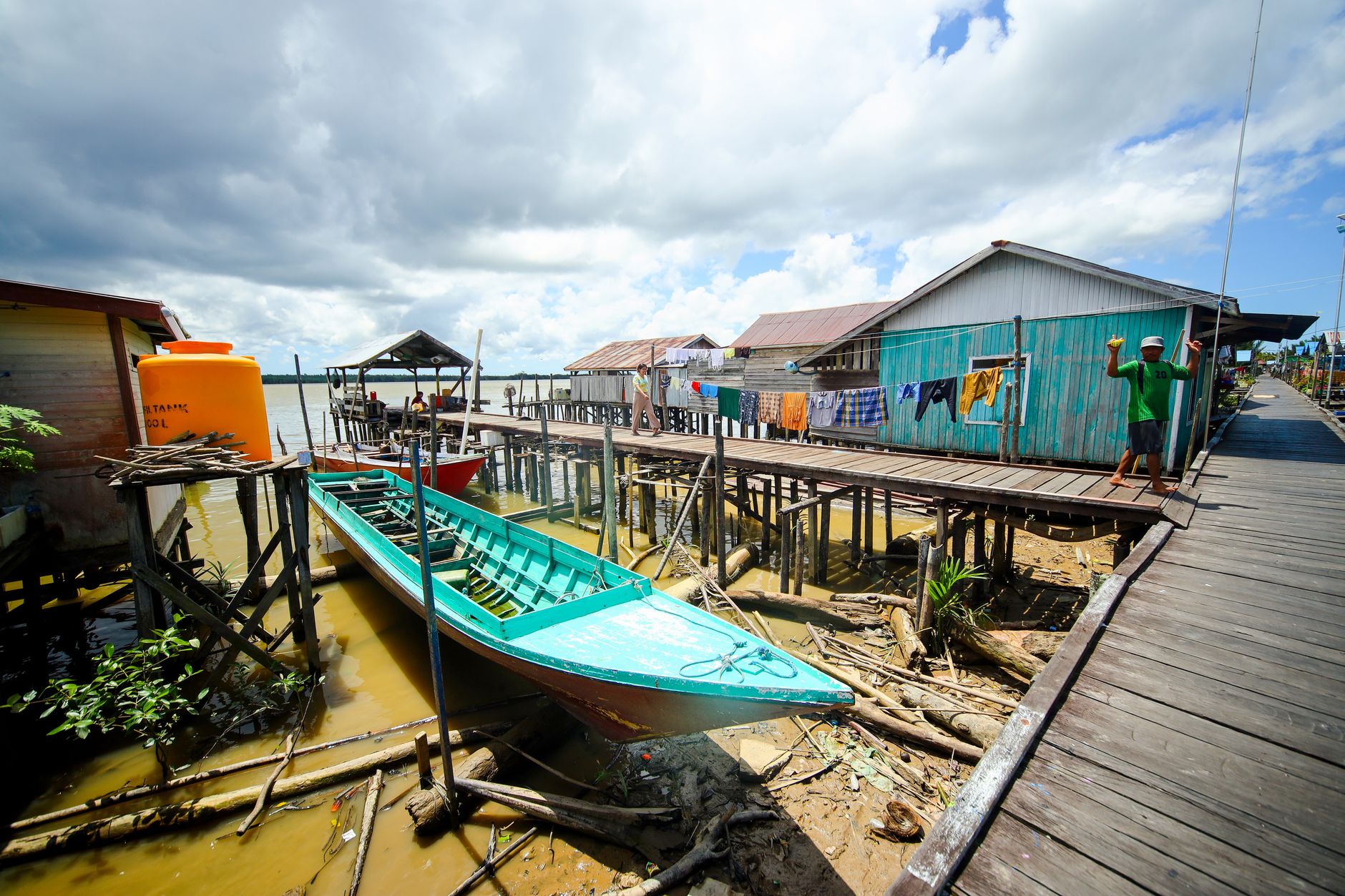 A longtail boat traveling along a remote river near a small village at forest edge
