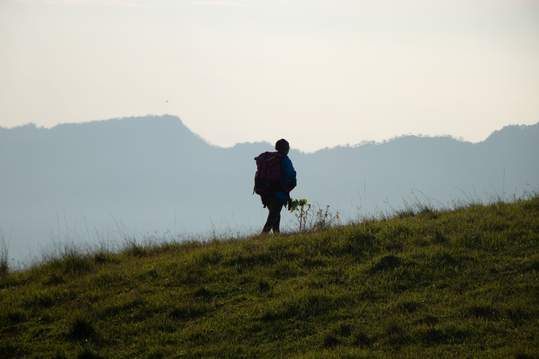 Solo hiker on a high-altitude trail at sunrise with valley views below