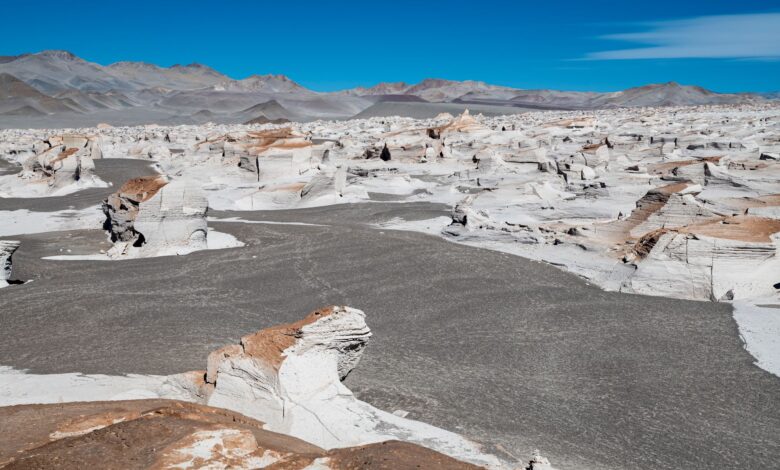 White chalk rock formations rising from a flat desert plain under a clear blue sky