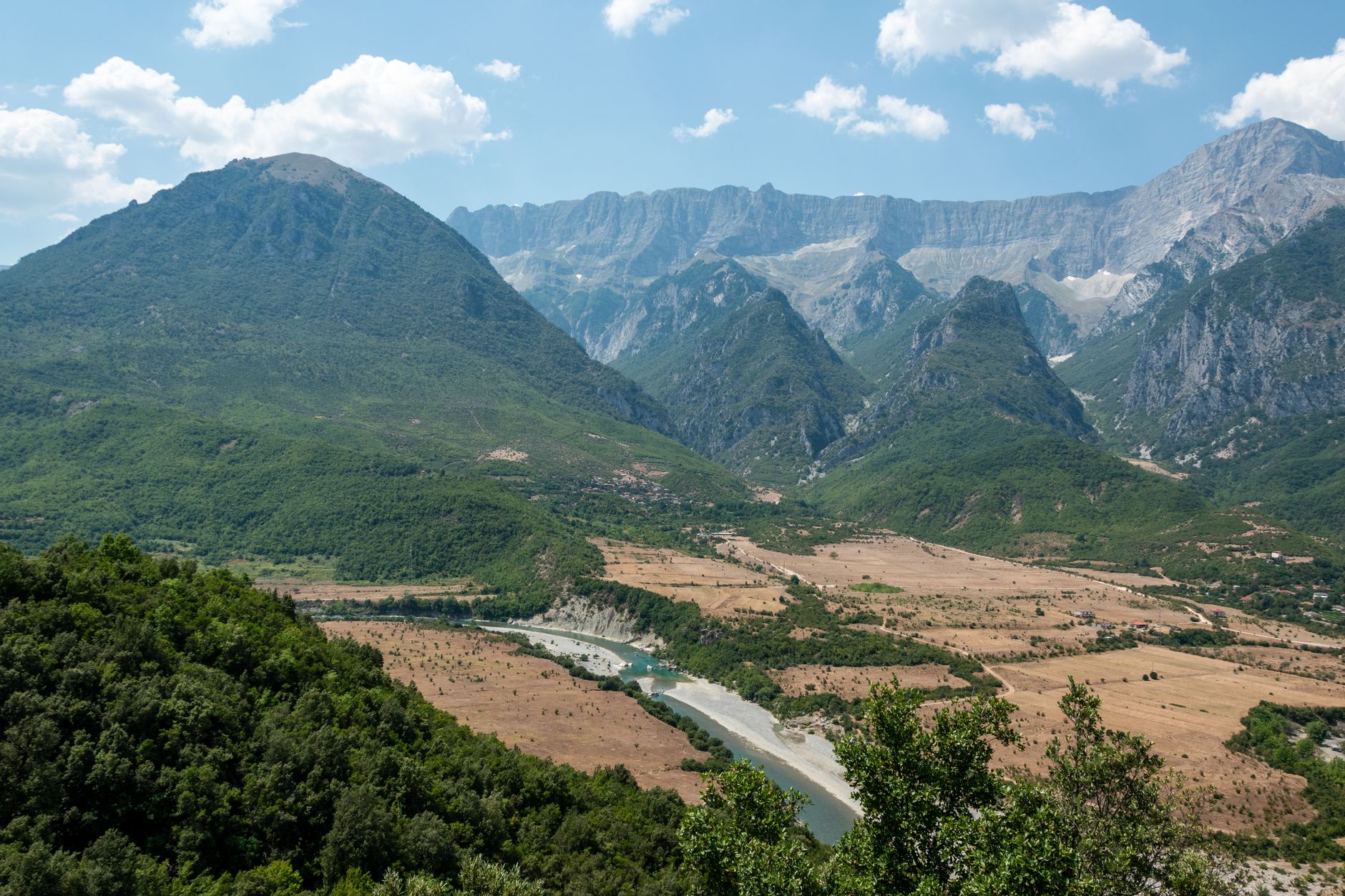 Wide view of a glacially carved alpine valley with turquoise river and forested peaks in the Albanian Alps