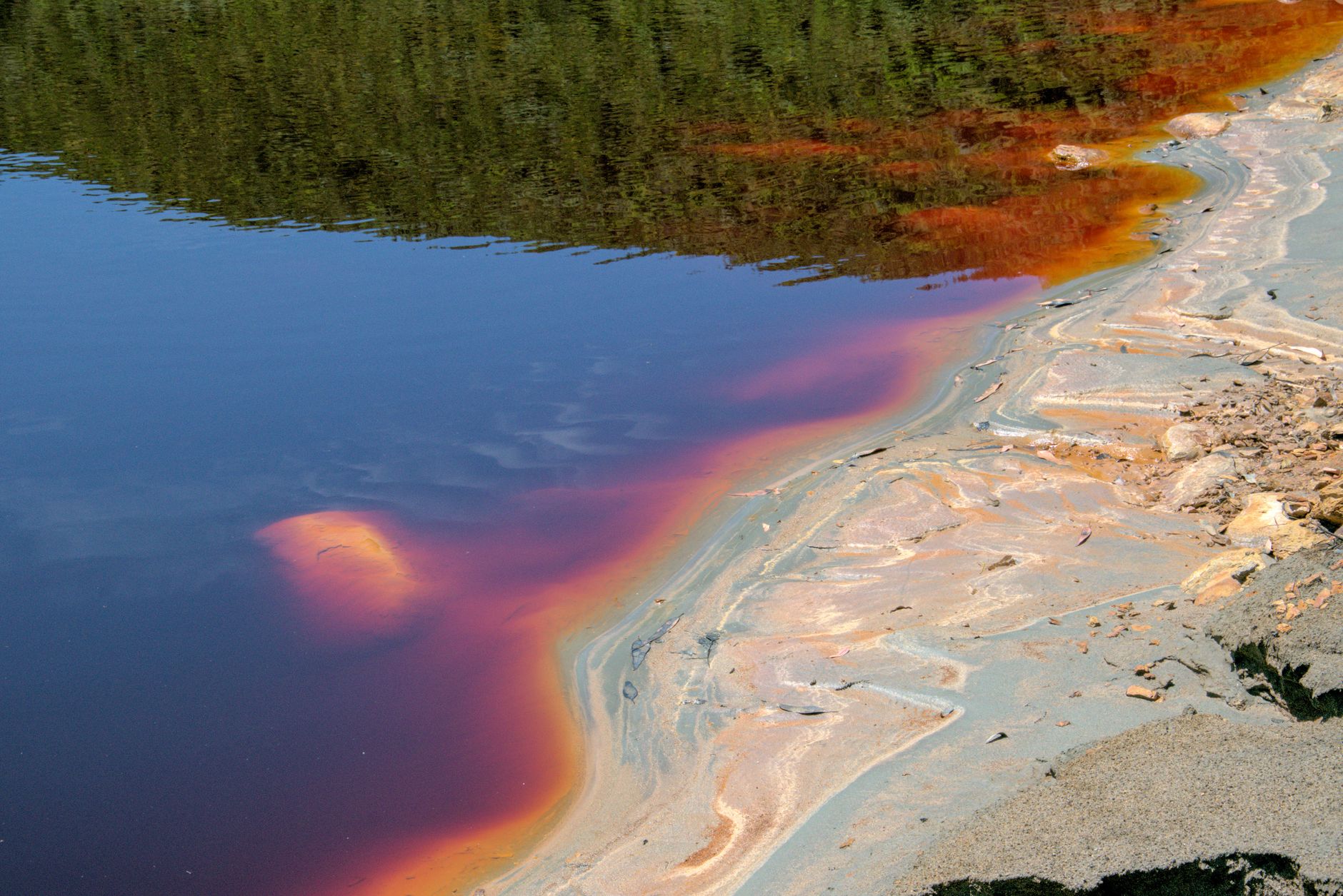 A shallow tropical river with vivid red and orange hues across the rocky riverbed
