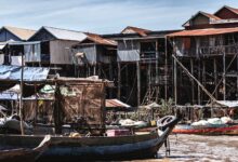 Wooden stilt houses built over a calm lake with misty mountains in the background