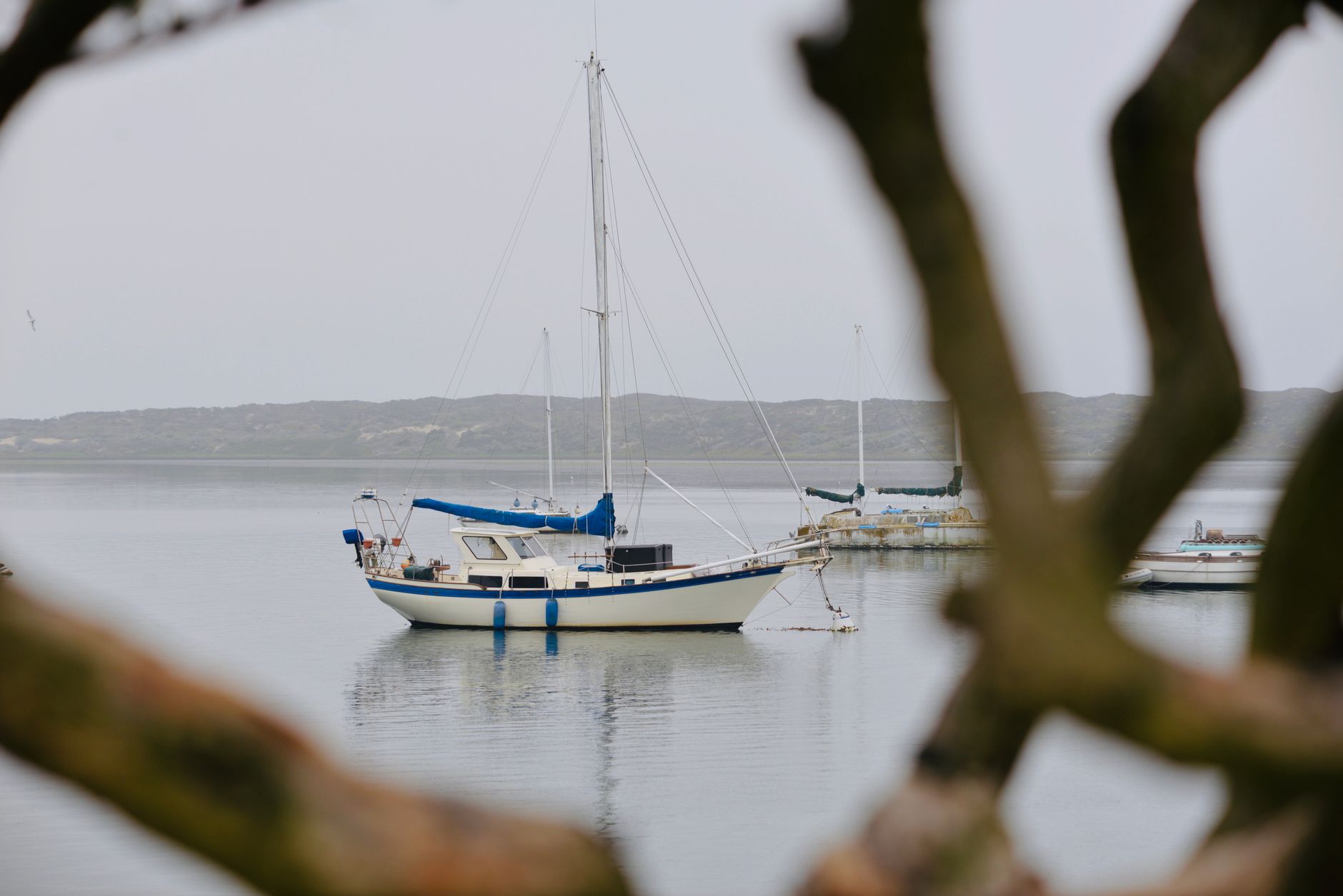 Sailboat anchored in a clear-water bay with rocky hills visible on the horizon