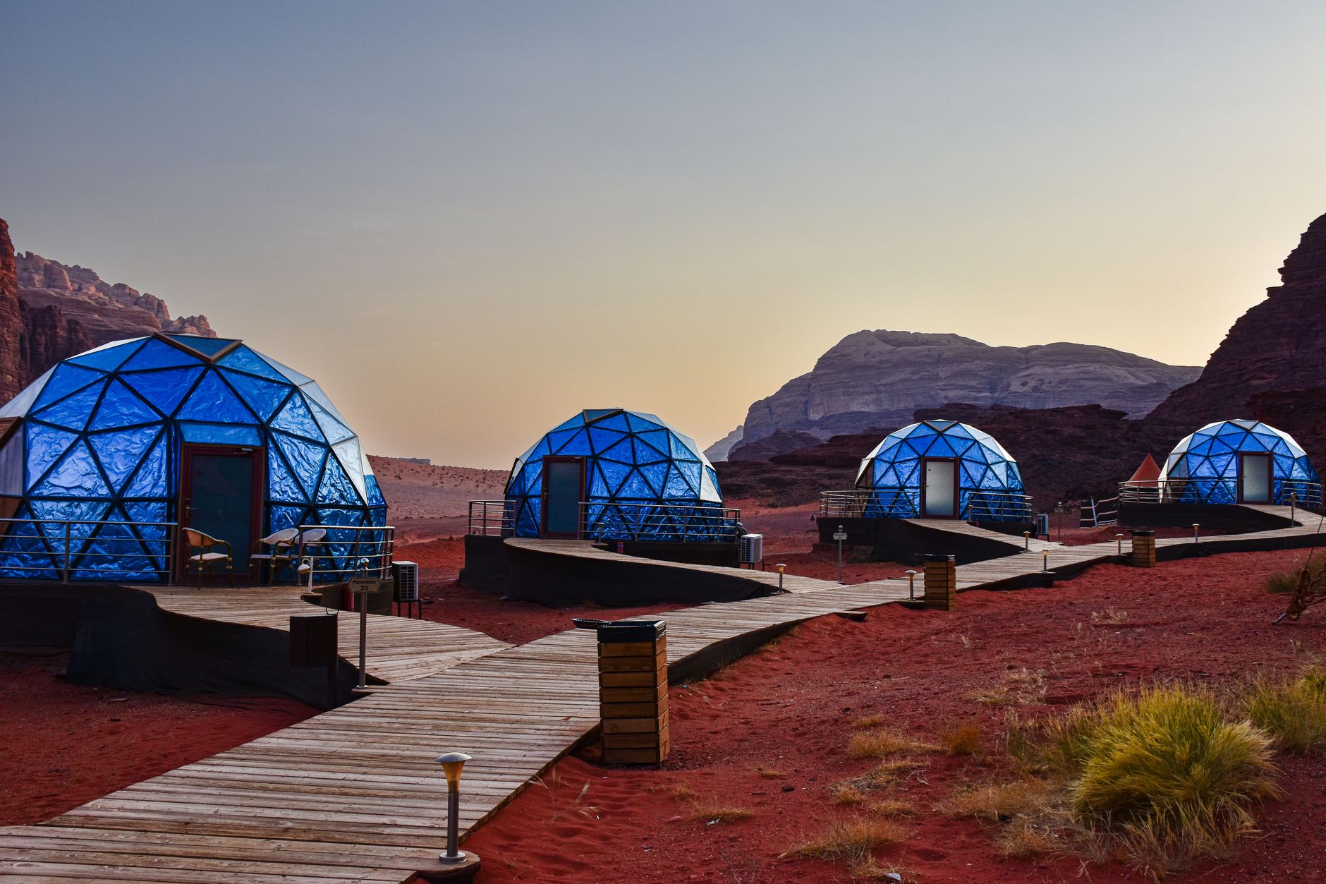 Traditional desert camp with canvas tents set against towering red rock walls at dusk