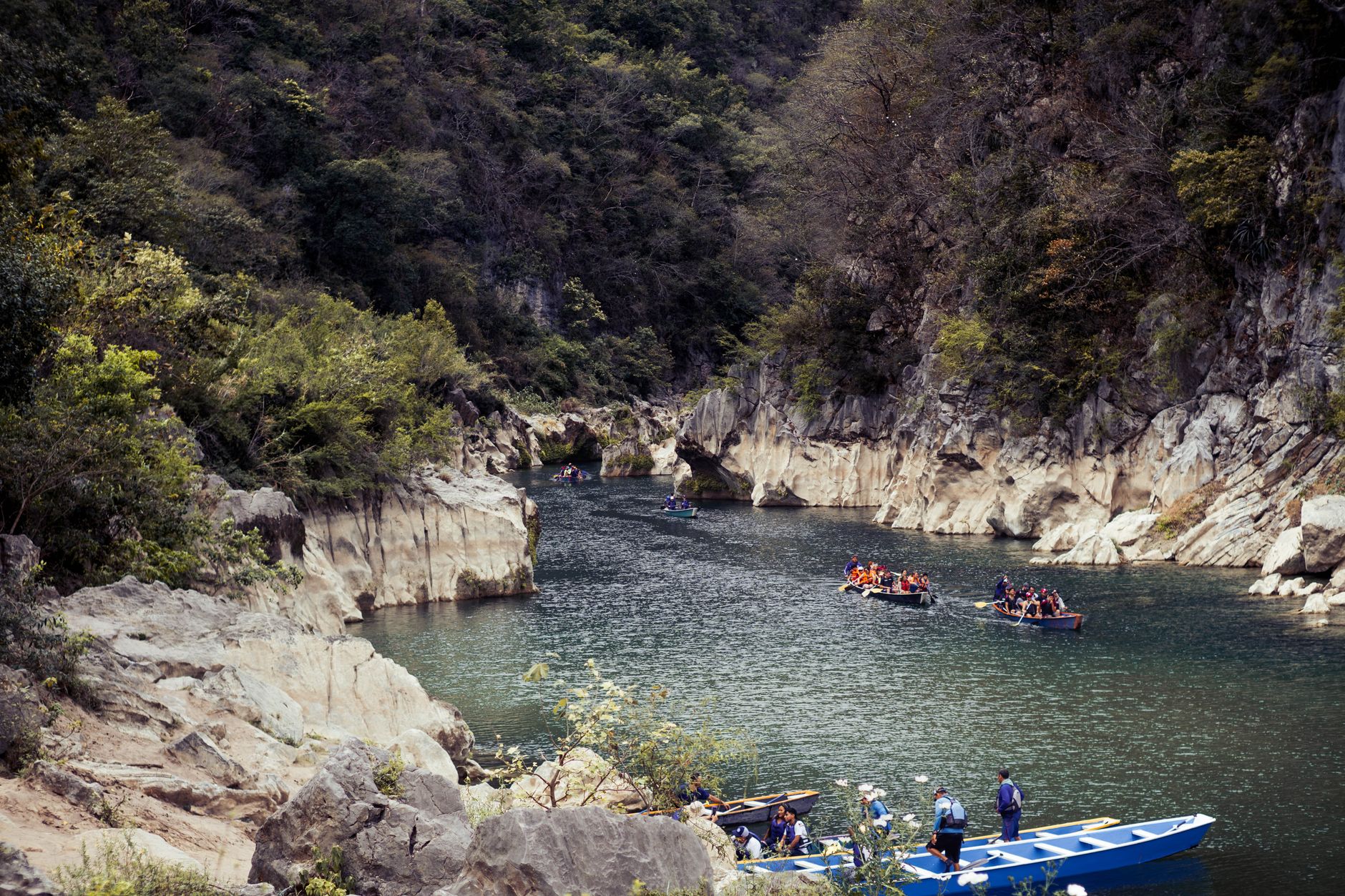 Kayaker navigating a narrow river canyon with steep limestone walls and clear green water
