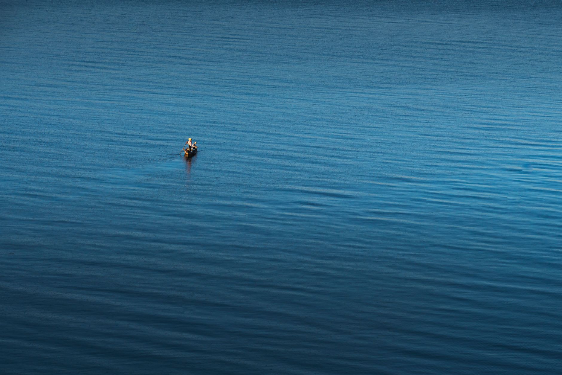 A fisherman standing on a wooden boat using a traditional rowing technique on a still lake