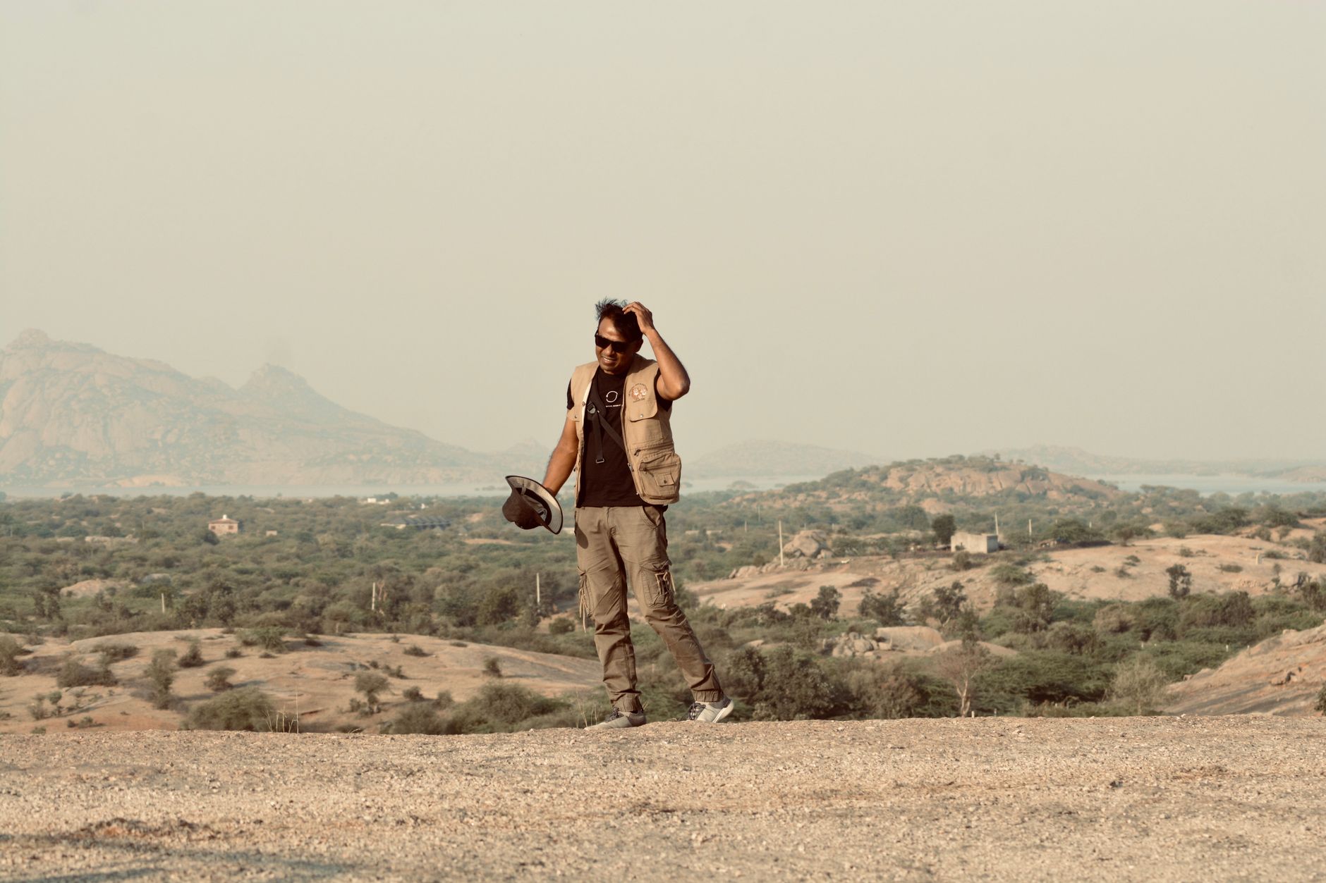 Solo trekker walking along a dry desert trail with dramatic Himalayan peaks visible in the background