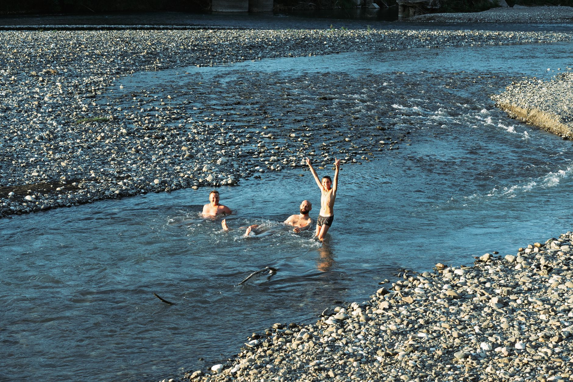 Visitors wading through clear shallow river water surrounded by lush green vegetation
