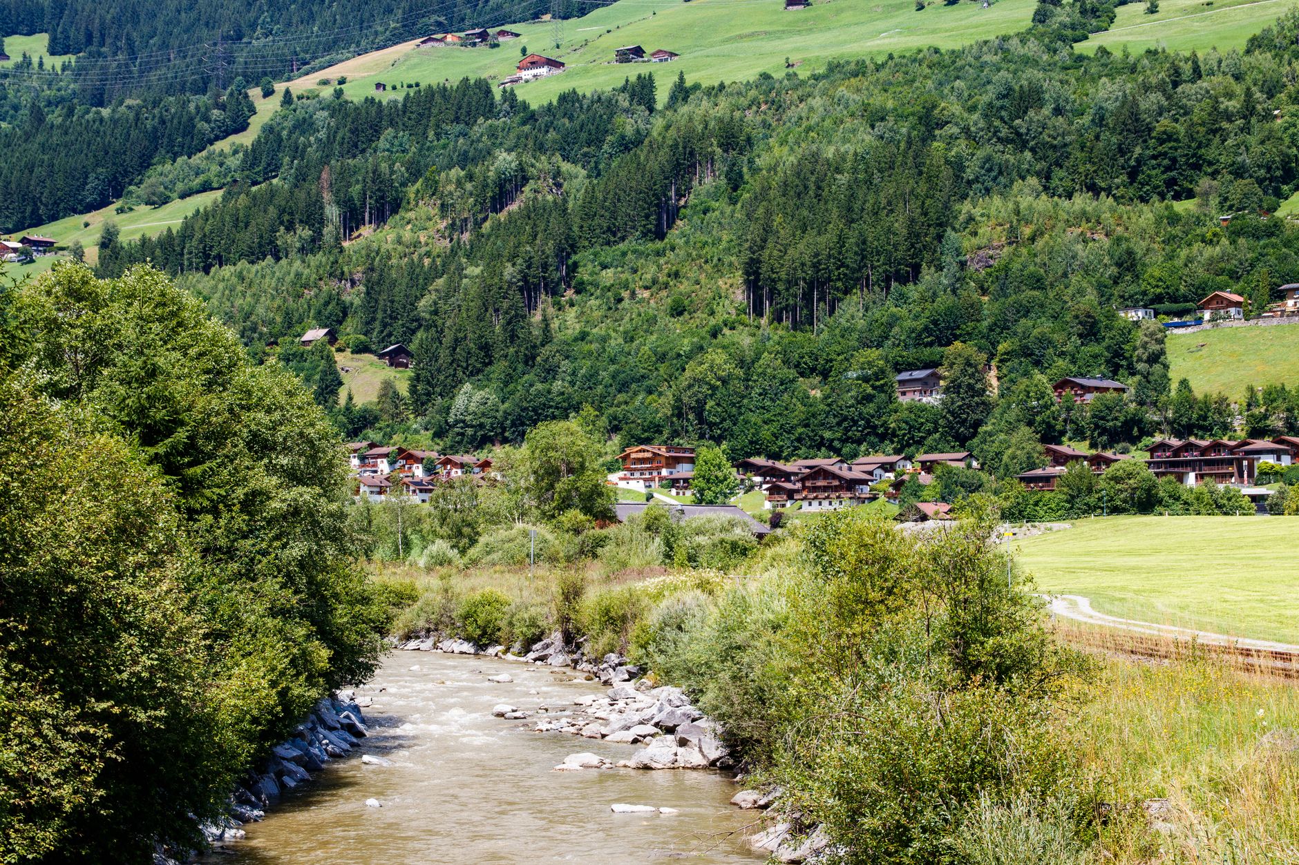 Small mountain village along a clear river valley with forested slopes in the background