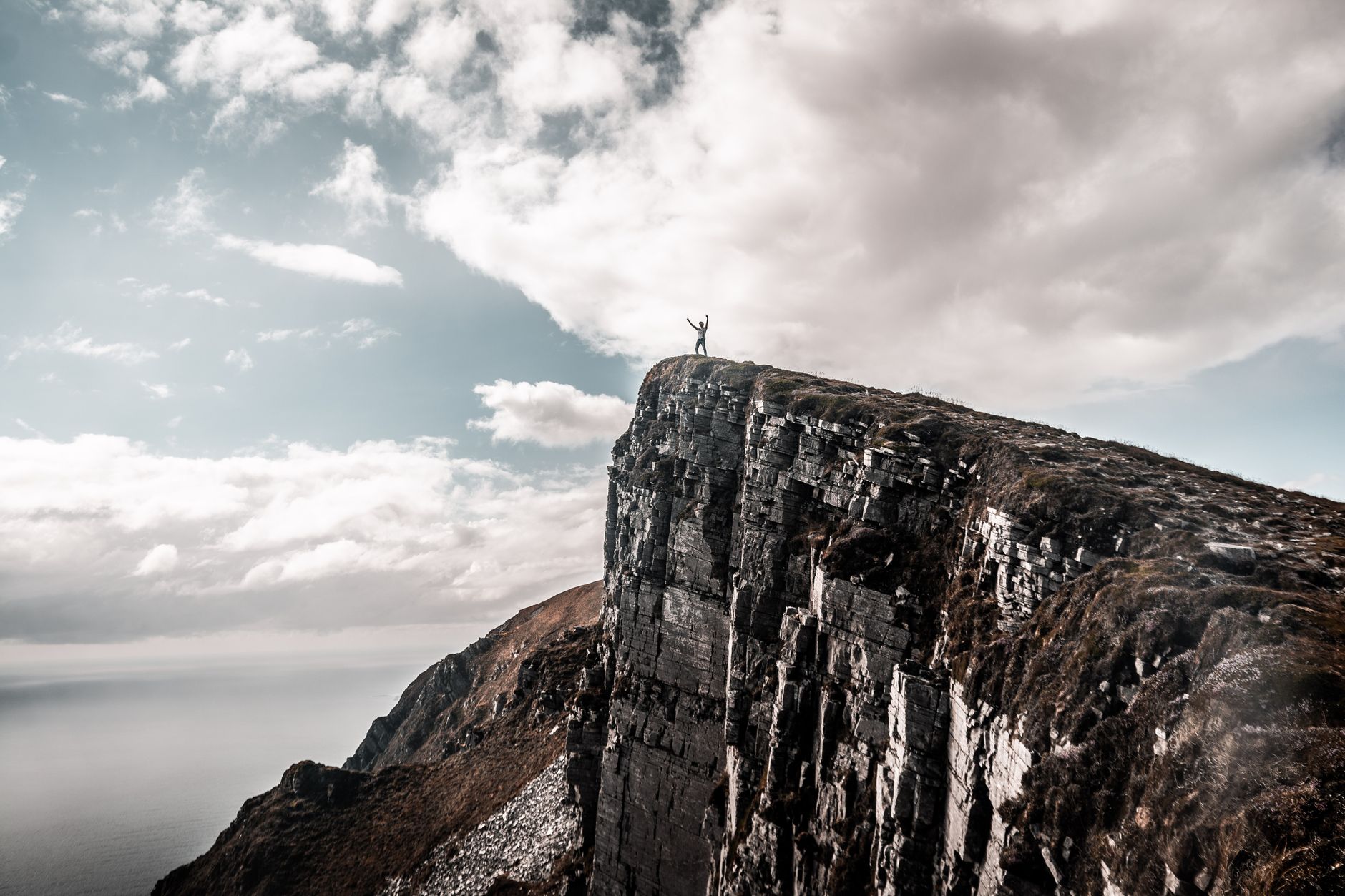 A hiker standing near the edge of a steep coastal cliff overlooking the sea