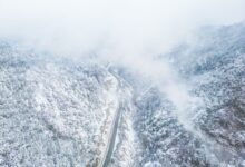 A narrow mountain road disappearing into thick cloud and fog on a steep Andean slope