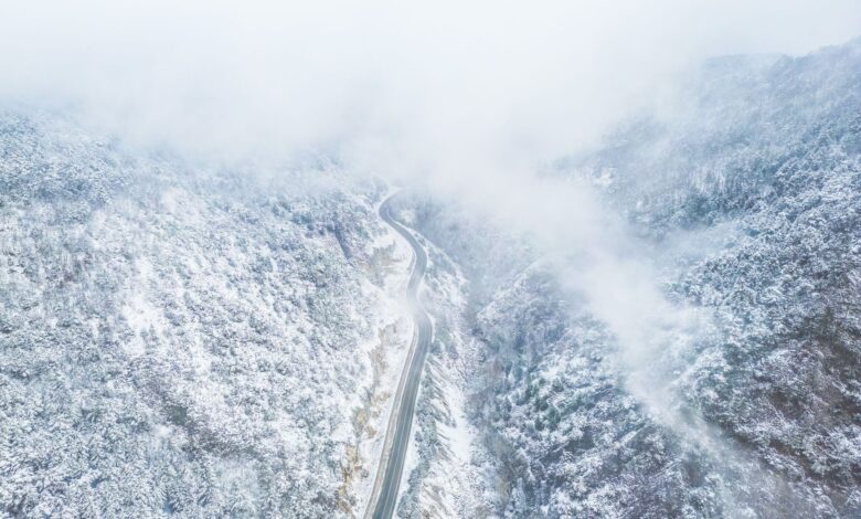 A narrow mountain road disappearing into thick cloud and fog on a steep Andean slope