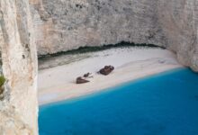 A rusted shipwreck sitting on a remote Atlantic coastline with desert sand dunes in the background