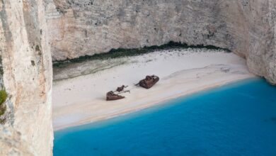 A rusted shipwreck sitting on a remote Atlantic coastline with desert sand dunes in the background