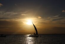 A traditional wooden dhow sailing on calm Indian Ocean waters near an archipelago coastline