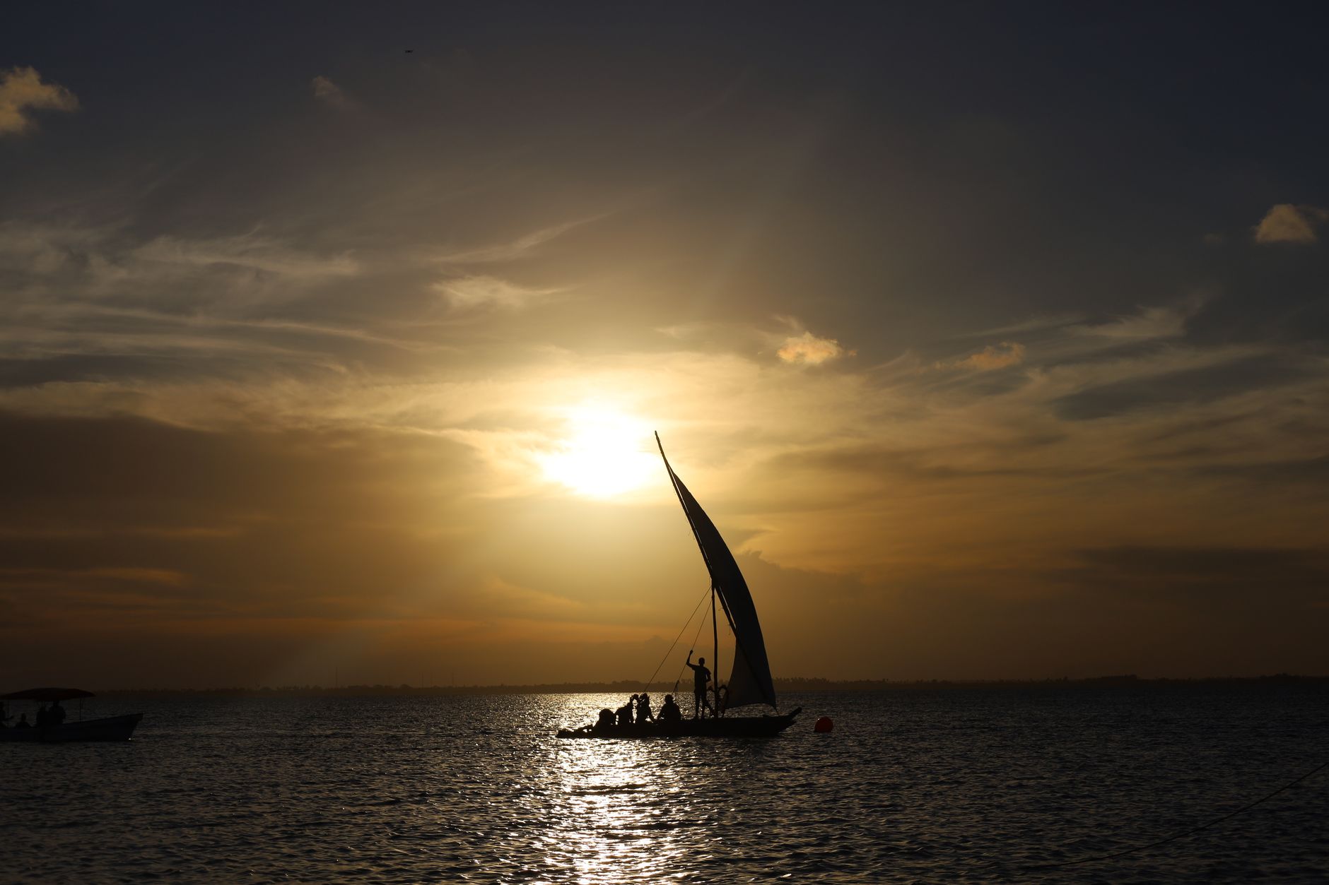 A traditional wooden dhow sailing on calm Indian Ocean waters near an archipelago coastline