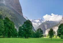 A wide alpine valley surrounded by dramatic limestone peaks under clear blue sky