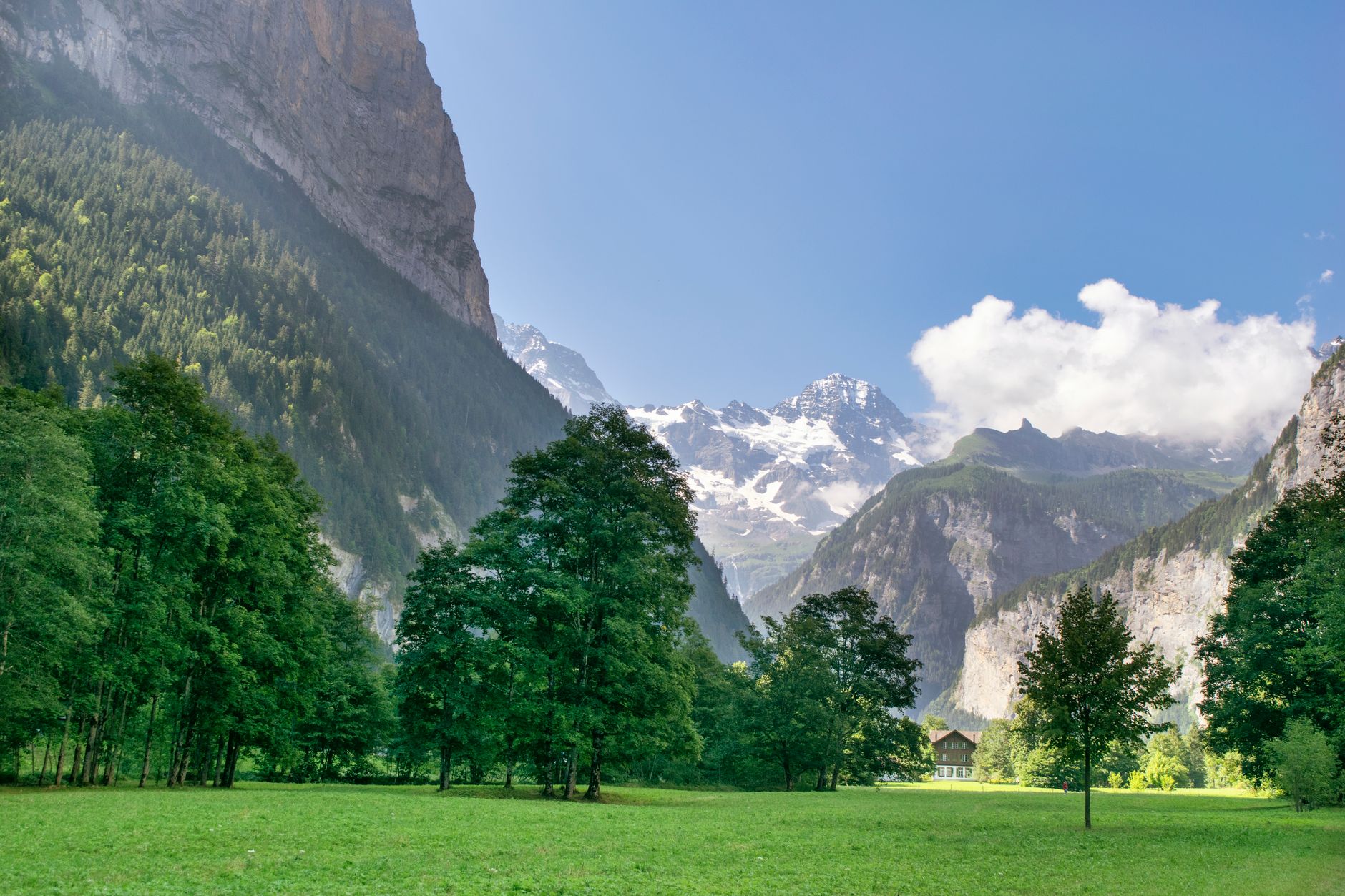 A wide alpine valley surrounded by dramatic limestone peaks under clear blue sky