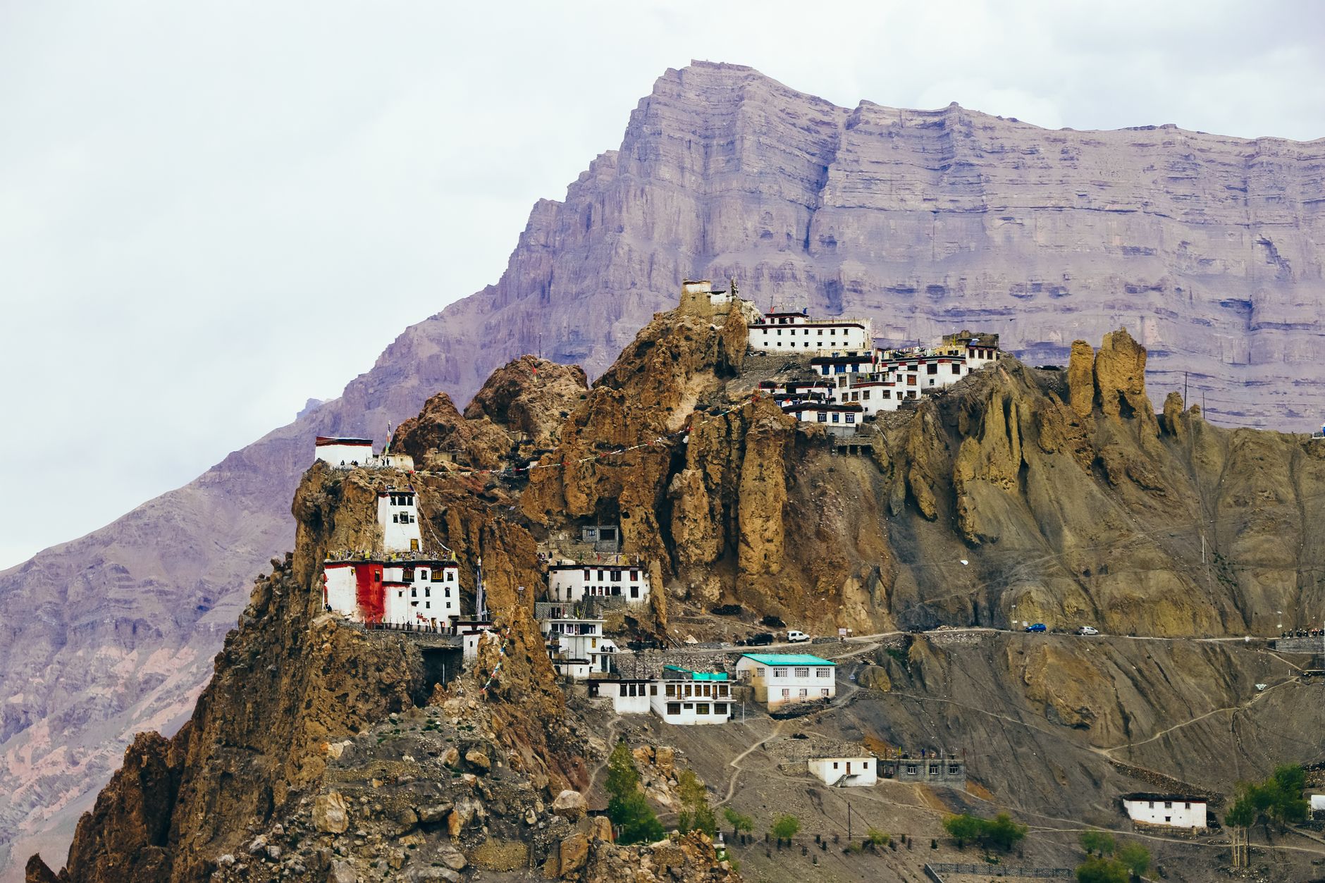 Ancient Buddhist monastery perched on a rocky outcrop above a remote mountain valley with prayer flags visible