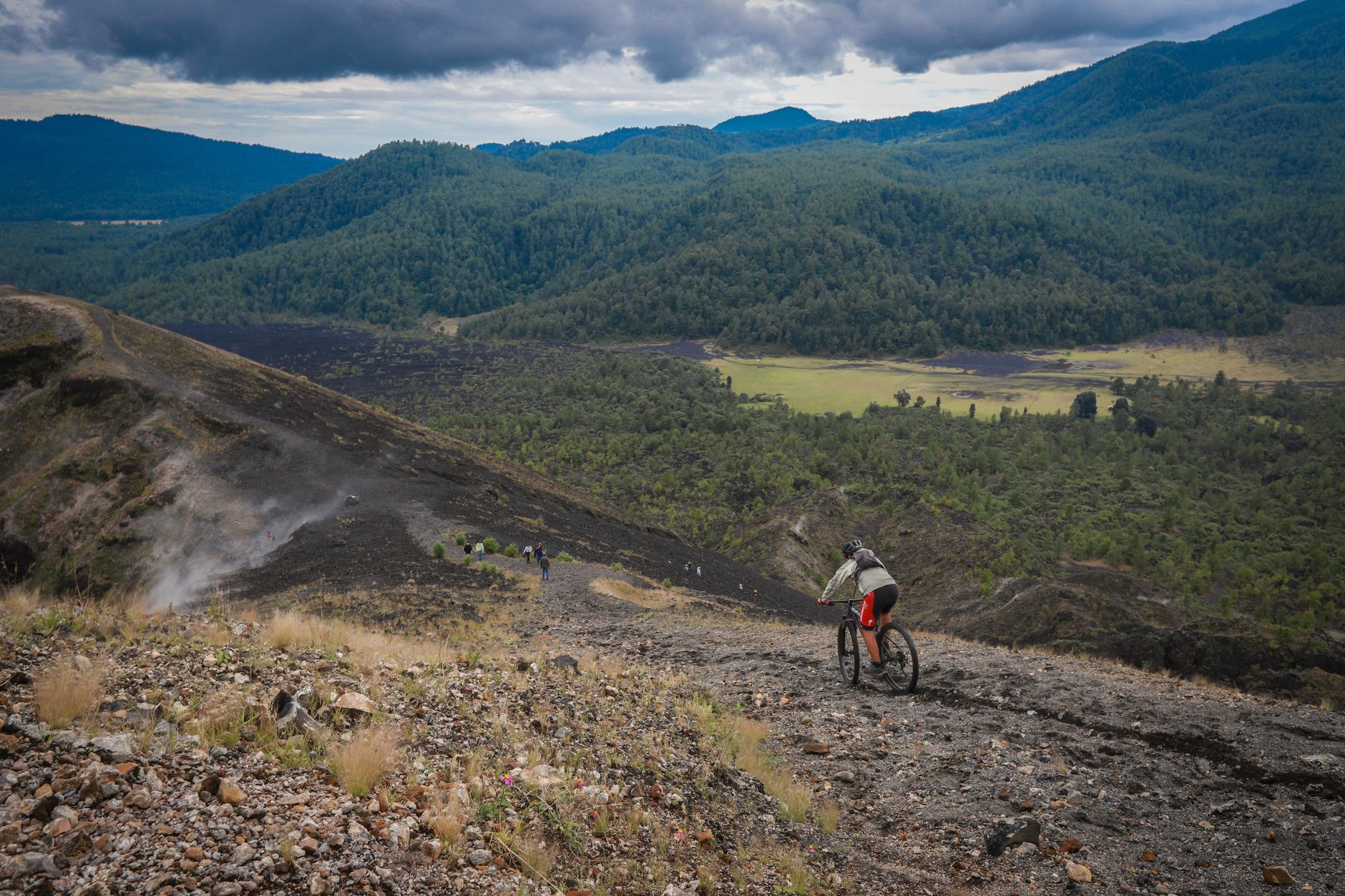 A cyclist descending a rugged mountain trail surrounded by dense green vegetation
